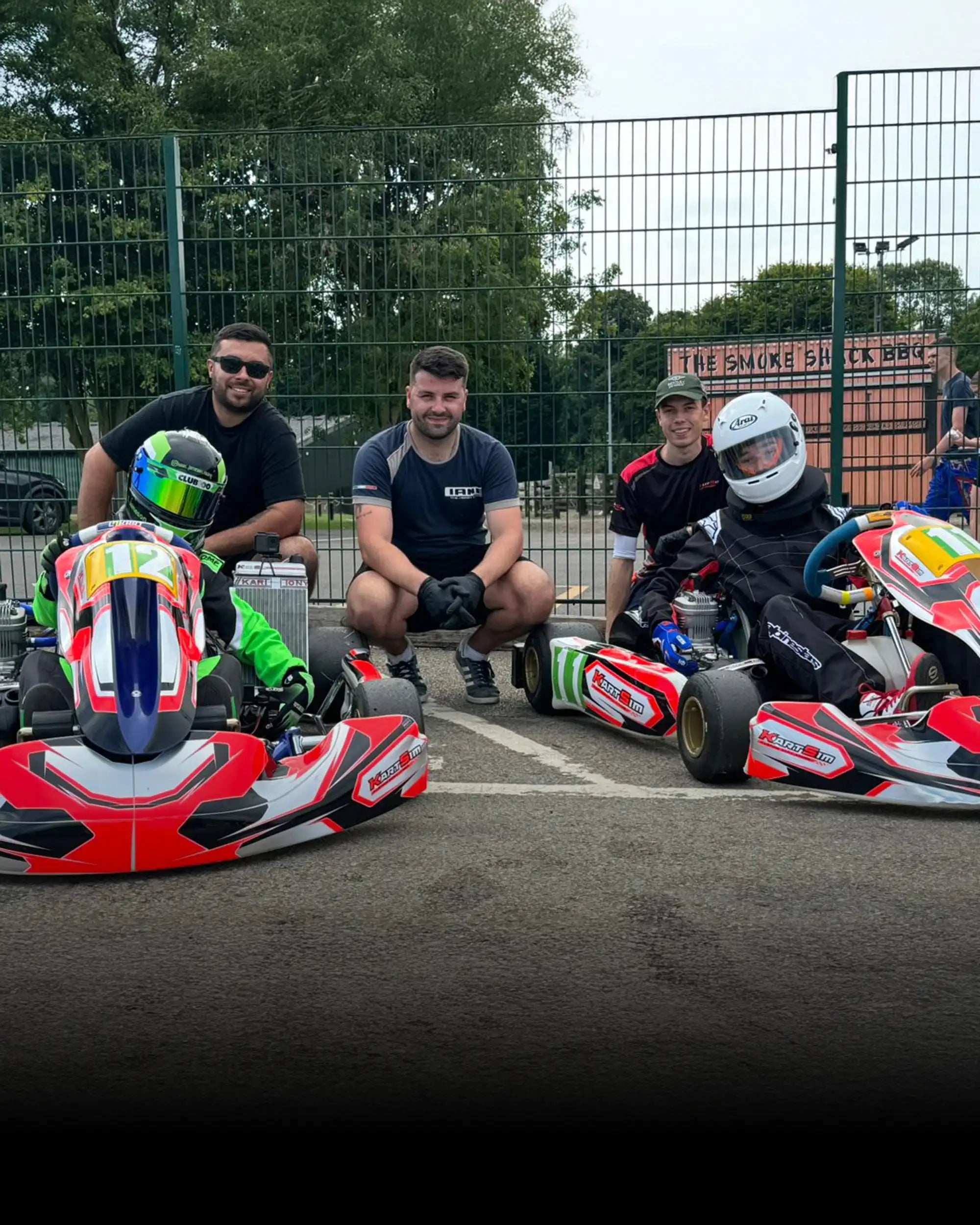 Two kart racing drivers in full gear with karts and professional driver coaching team outdoors