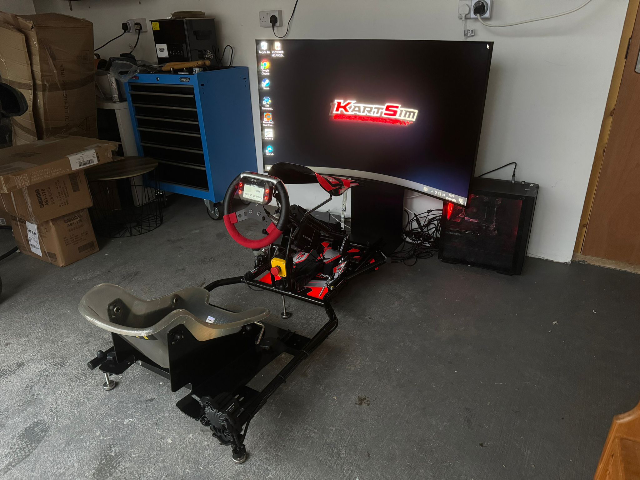 KartSim Pro Simulator set up in a home garage, featuring a full kart chassis and curved display for advanced home karting simulation.