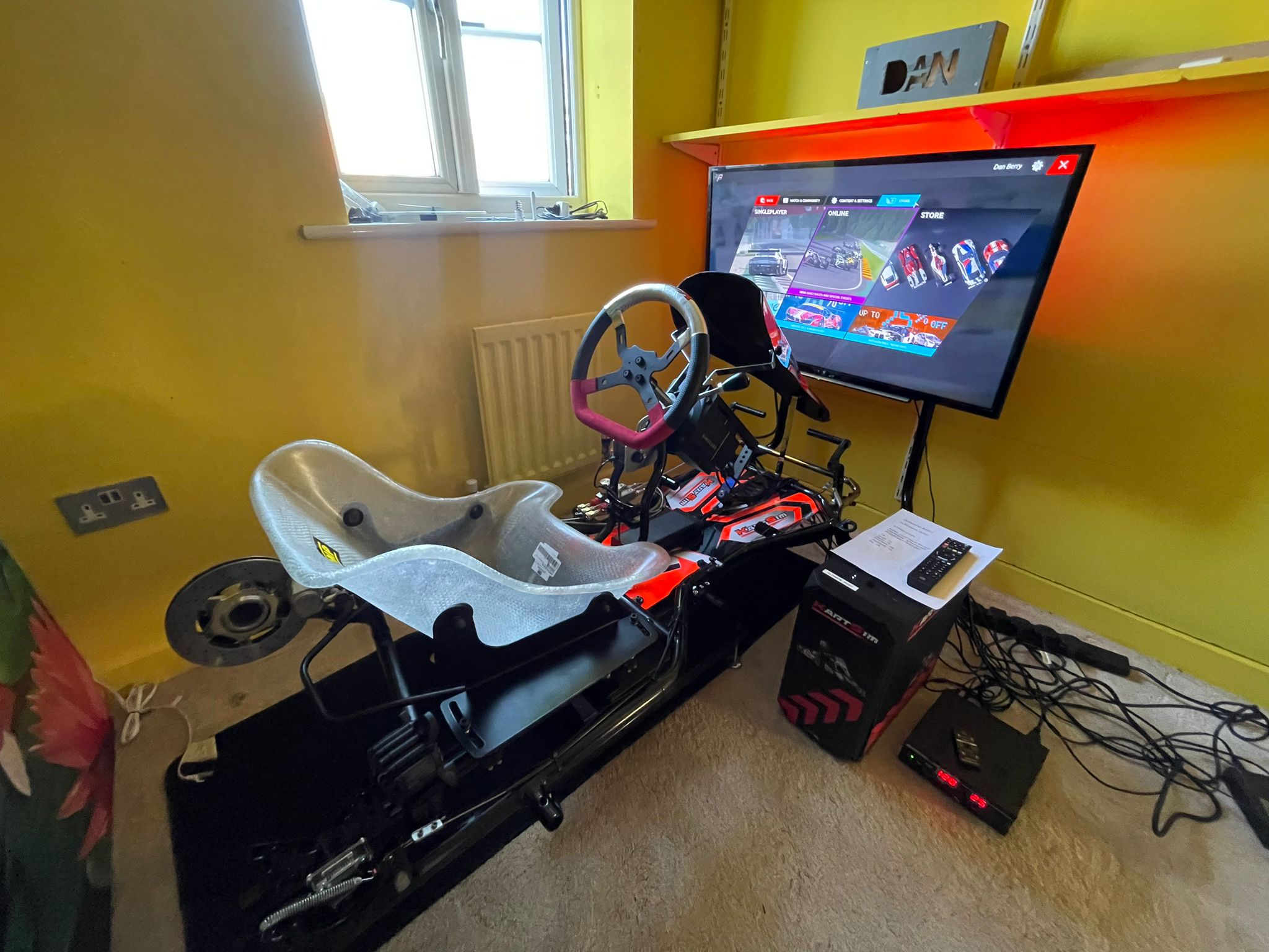 KartSim Pro Simulator set up against a bright yellow wall, highlighting the detailed kart seat and steering configuration.