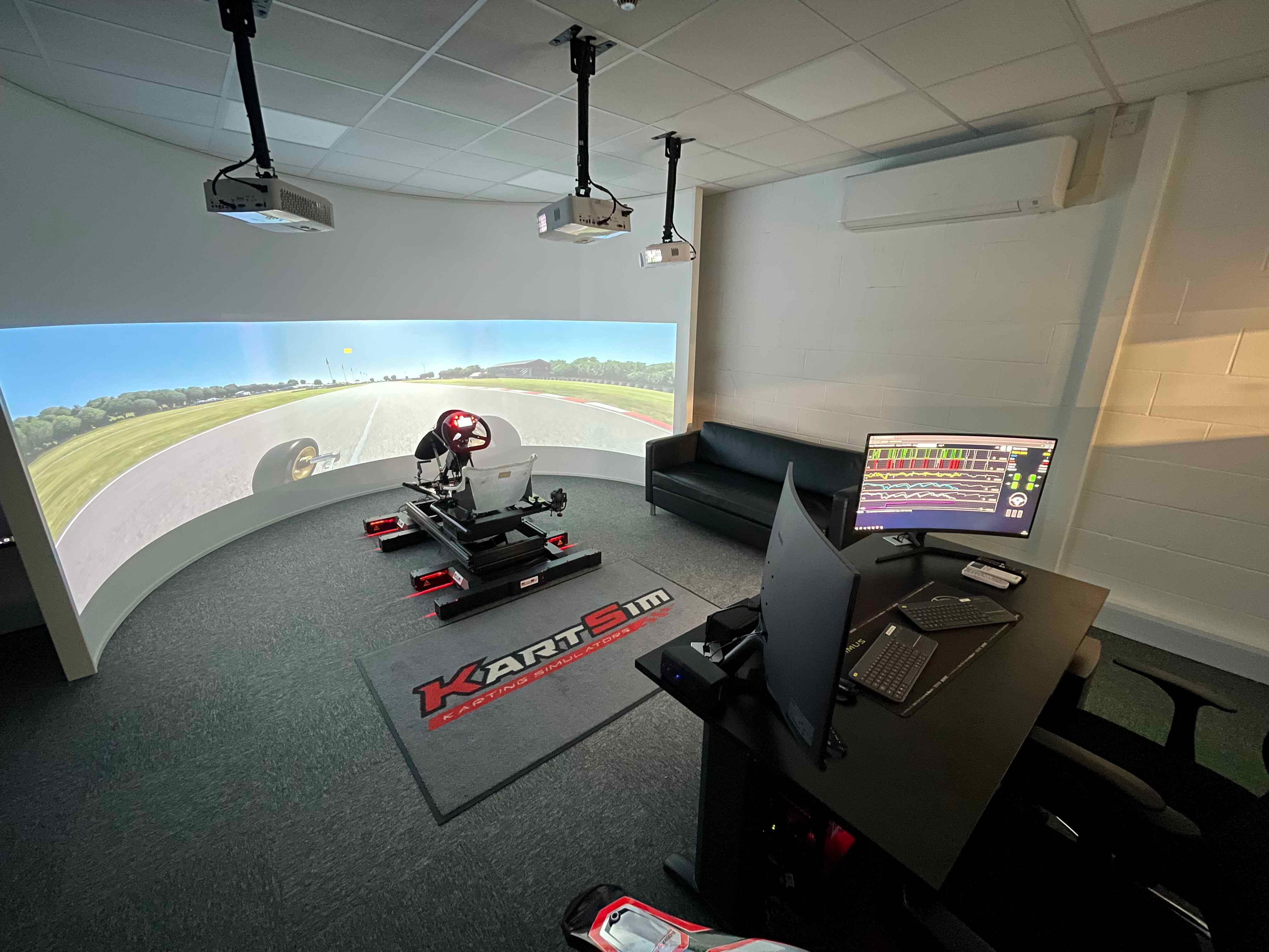 Professional kart racing simulator suite with curved screen, kart chassis, pedals, and live telemetry data analysis.