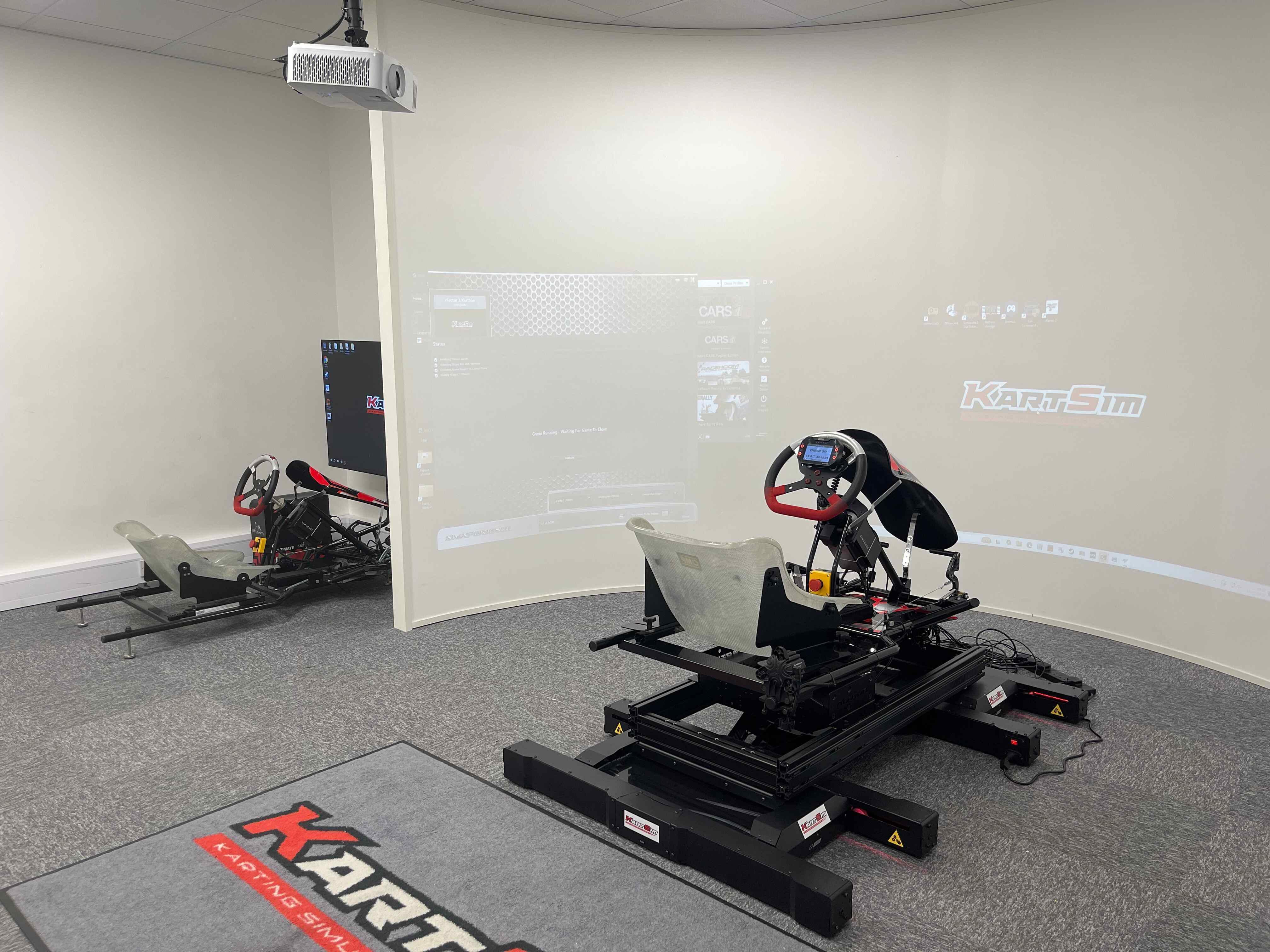 Professional KartSim dual full motion kart racing simulator setup with projection display, realistic seating and pedal positions for advanced karting training.