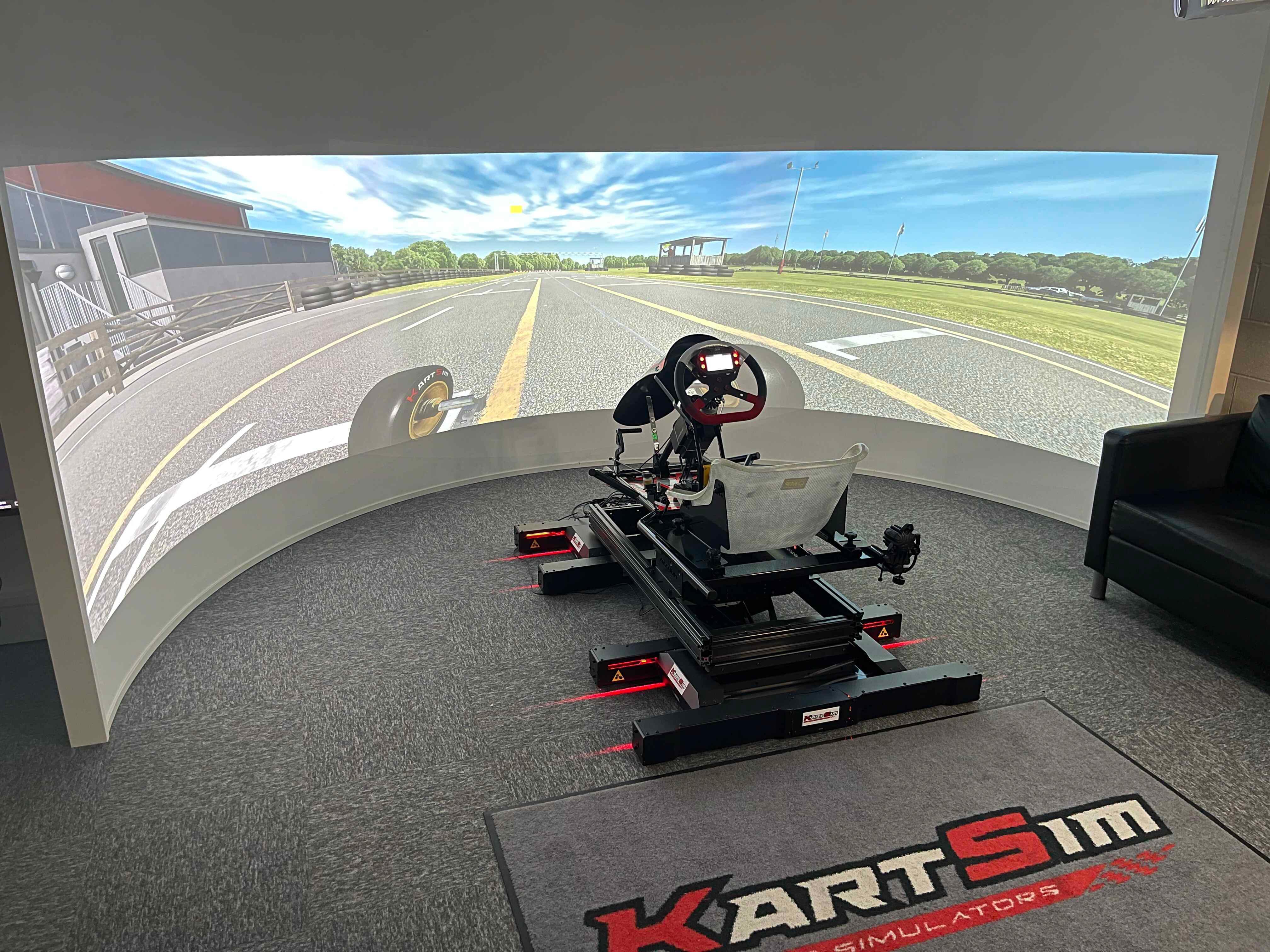 Full-motion kart racing simulator rig with curved projection display for professional karting training.