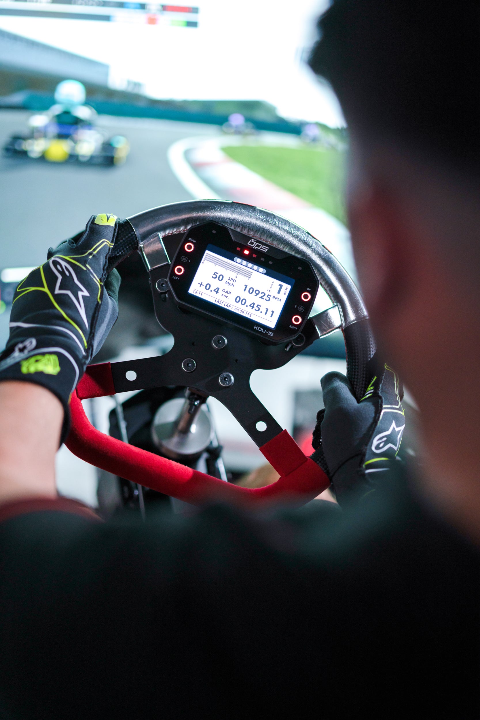 Close-up view of a kart racing steering wheel with digital GPS display showing speed, RPM, and lap time during race simulation