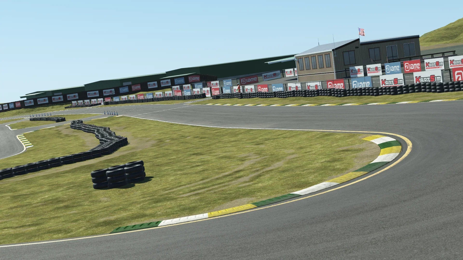 Trackside view of Sonoma karting circuit – corner entry with green-yellow curbing, tire walls, sponsor banners, and race control building