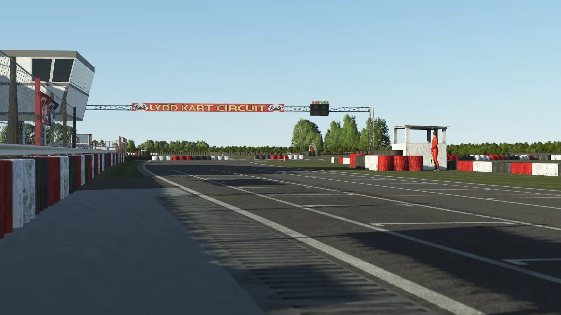 Low-angle view down the Lydd start/finish straight in KartSim, highlighting the tower, marshal post, and grid markings.