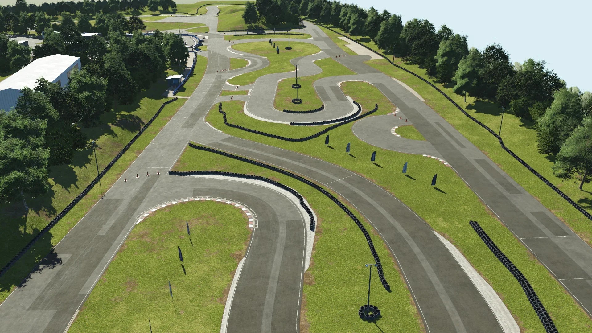 Aerial view of Teesside kart circuit in KartSim, showing its long, winding layout bordered by trees, tyre barriers, and green grass, with multiple tight turns and straights visible under a bright sky.