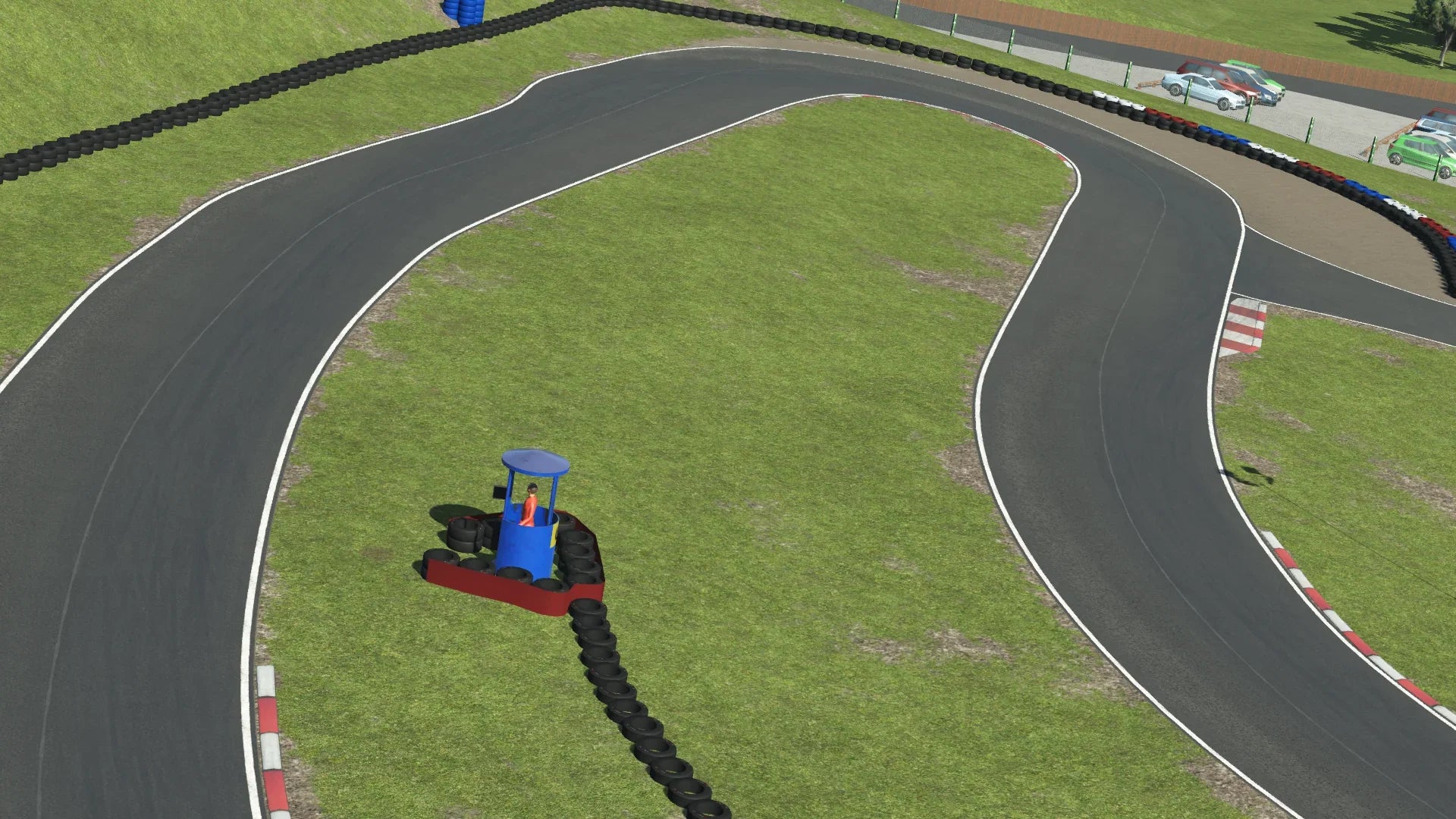 Wide-angle view of Warden Law kart circuit rendered in dry weather, showing a sweeping section of asphalt track lined with tyre barriers.