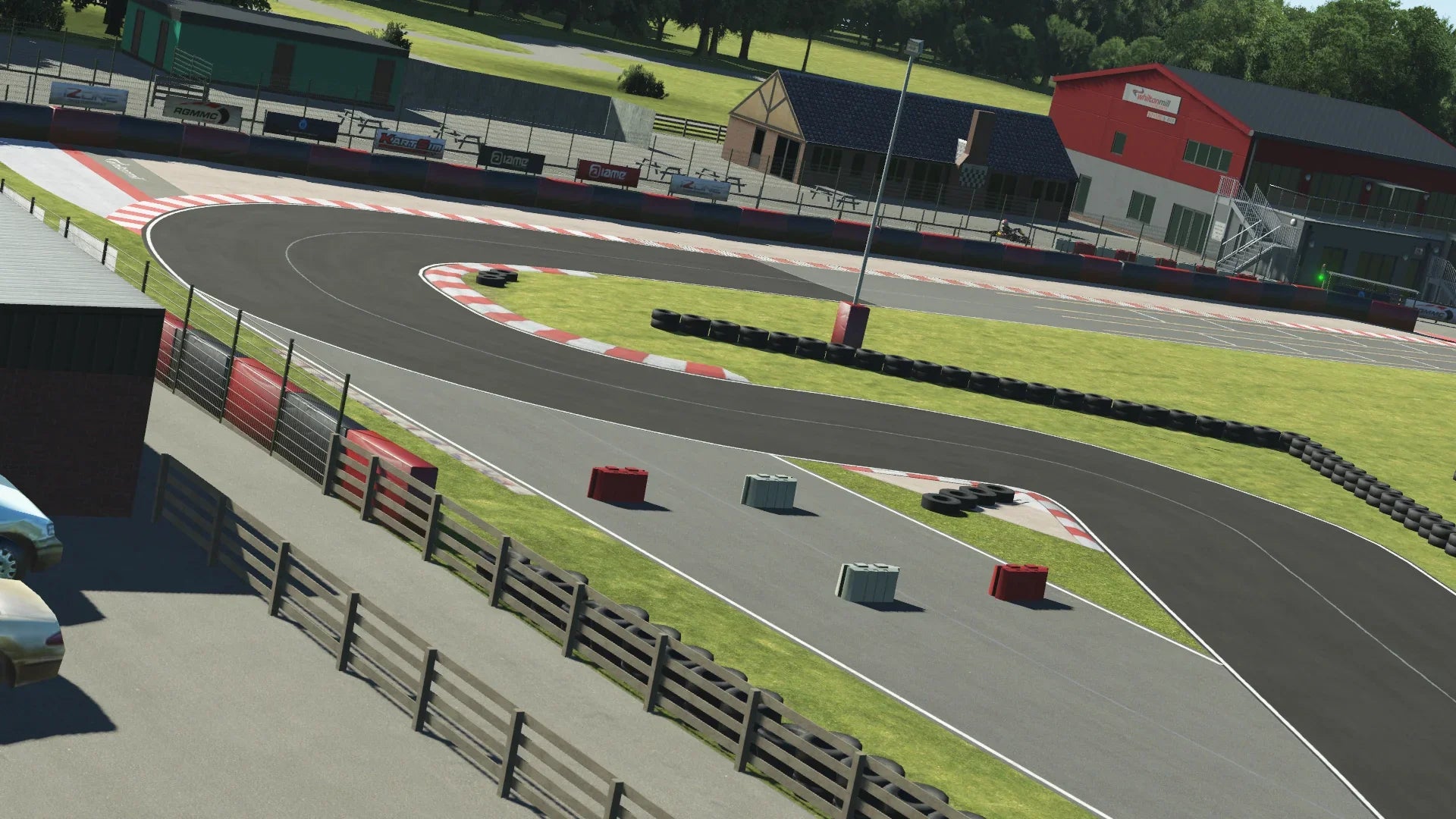 KartSim Whilton Mill track corner view – A sharp, technical corner at Whilton Mill, accurately recreated in KartSim, featuring red and white kerbs, tyre barriers, and the clubhouse in the background.