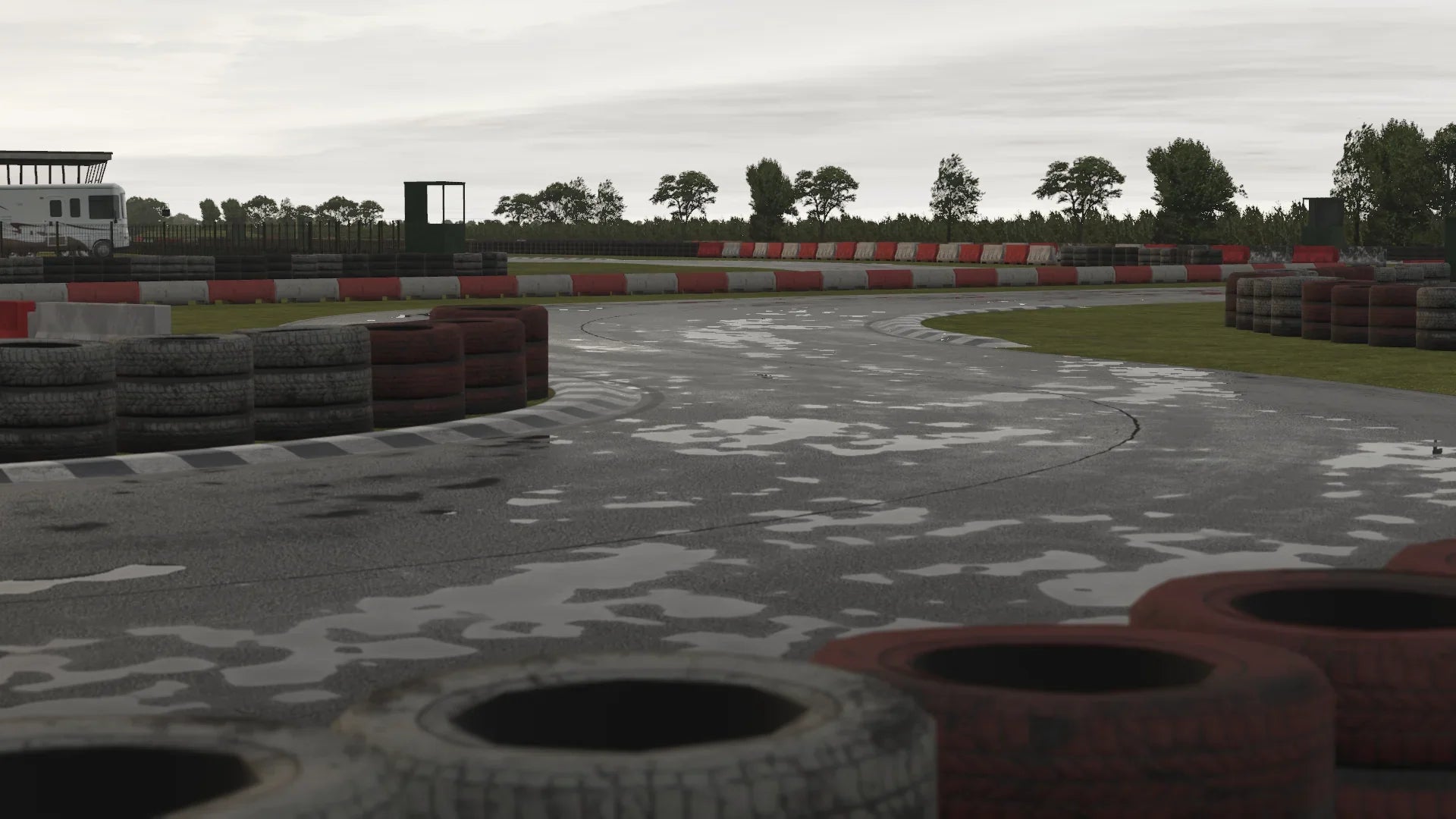 A soaked mid-corner section of Fulbeck with visible water pooling, painted curbs and tyre walls enclosing the circuit.