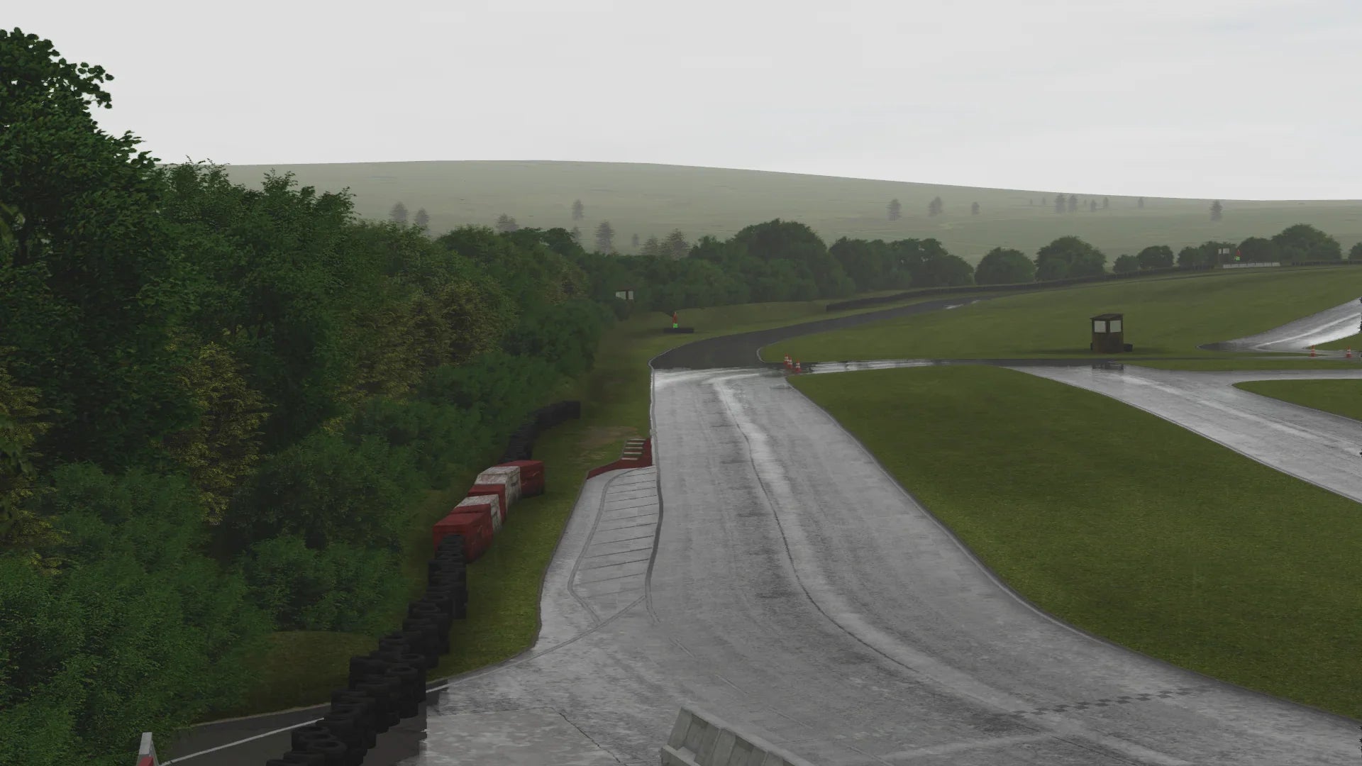 A wet race day at GYG – The KartSim recreation of Glan y Gors shows a rain-soaked uphill straight, bordered by trees and red-and-white tyre barriers, capturing the circuit’s challenging elevation changes.