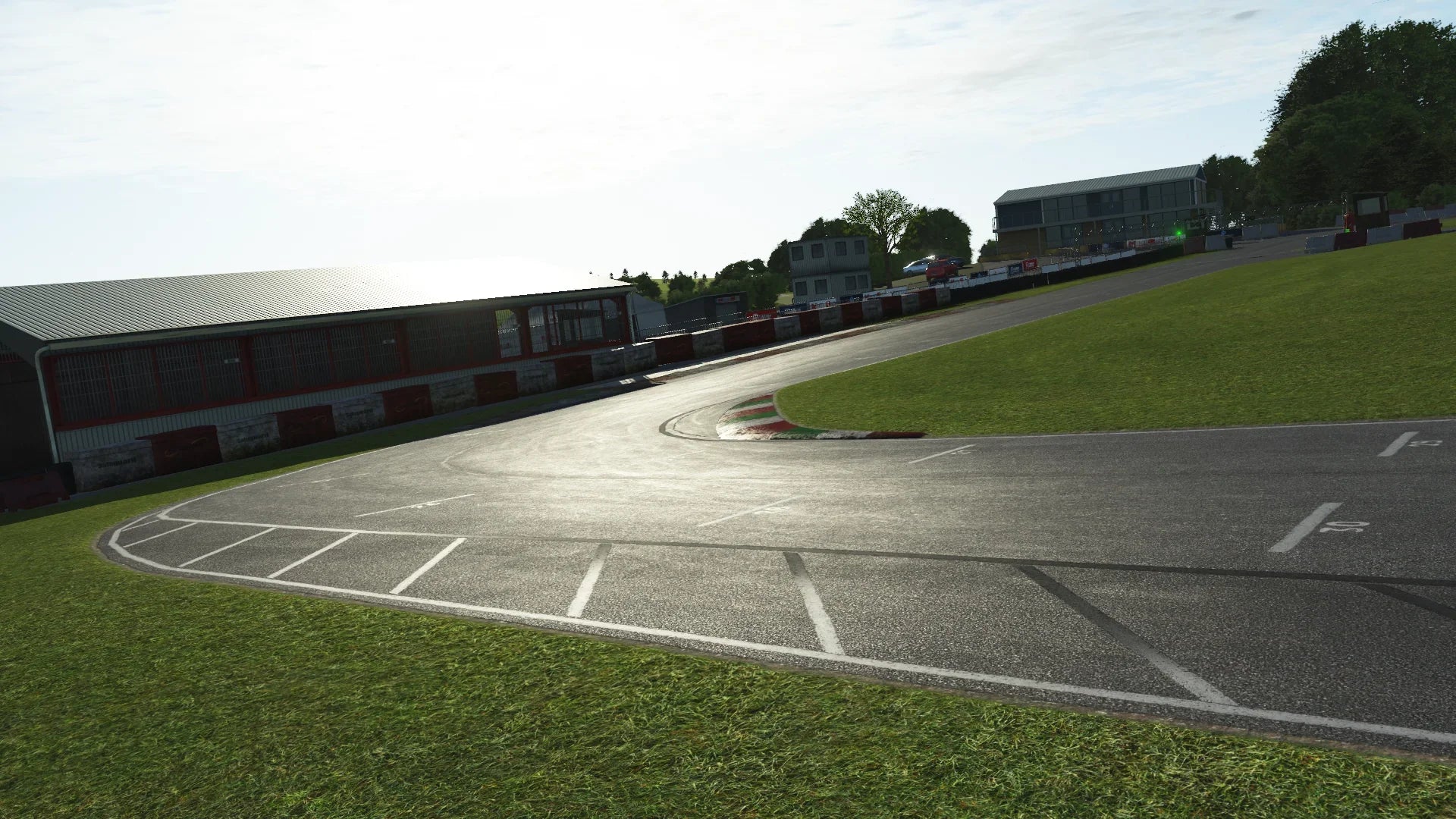 GYG pit straight and paddock – In KartSim, the main straight passes the large pit building and control tower, with the late-afternoon sun glinting off the slightly damp track surface.