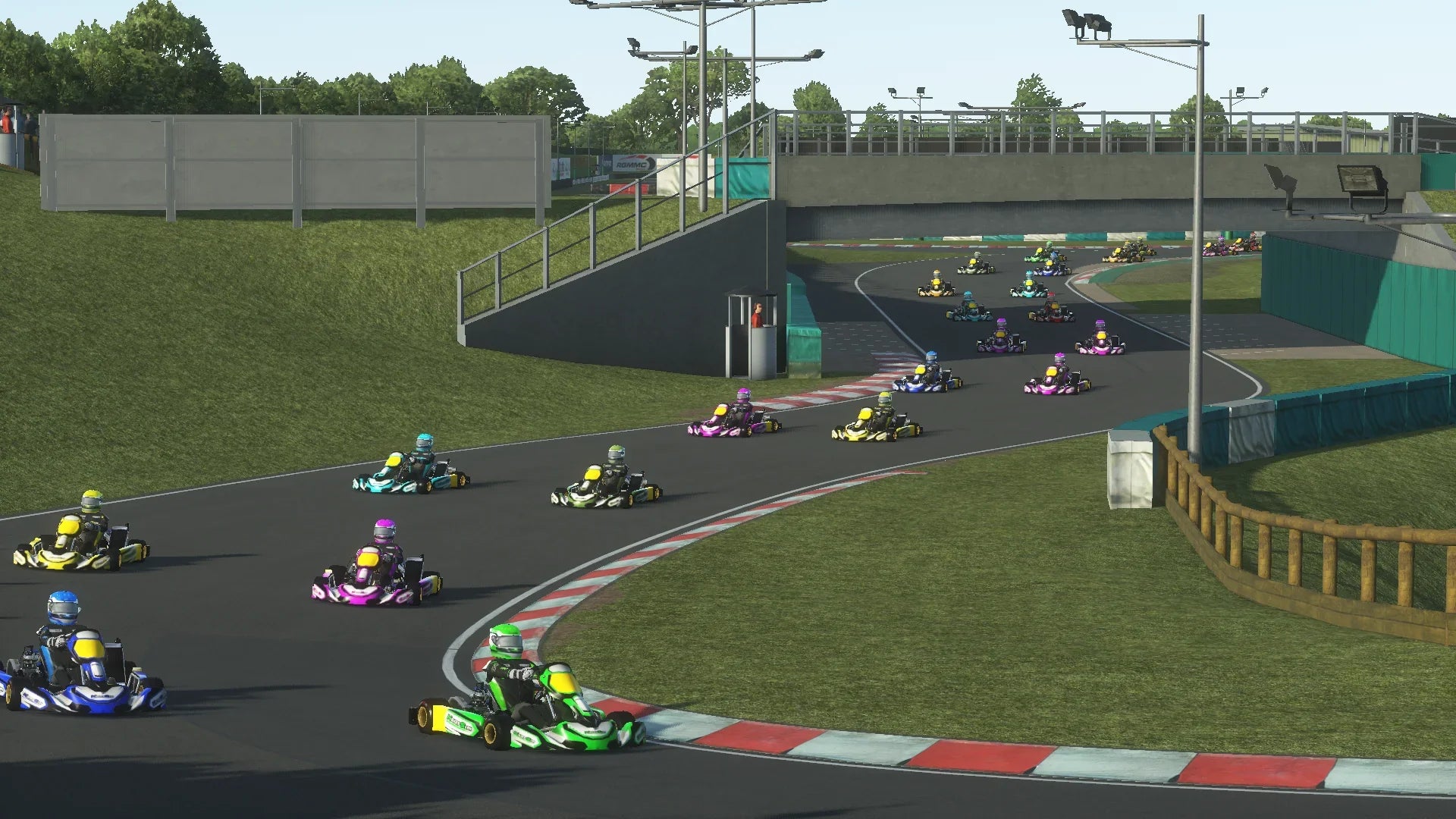 Colourful karts compete closely through PFI International’s technical section on KartSim, with the iconic bridge overhead and grandstands in the background.