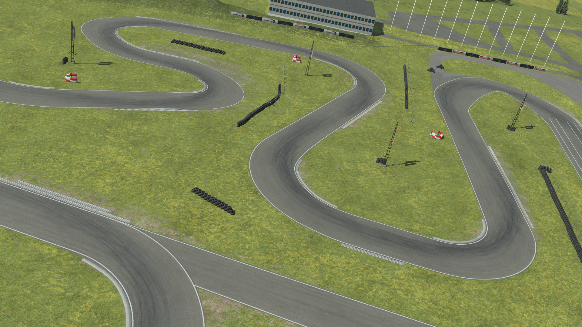 KartSim render of the Kristianstad circuit: a winding gray asphalt track weaving through a green grass infield, with scattered tire barriers, marshal posts, and a multi-storey paddock building and flagpoles visible in the background.