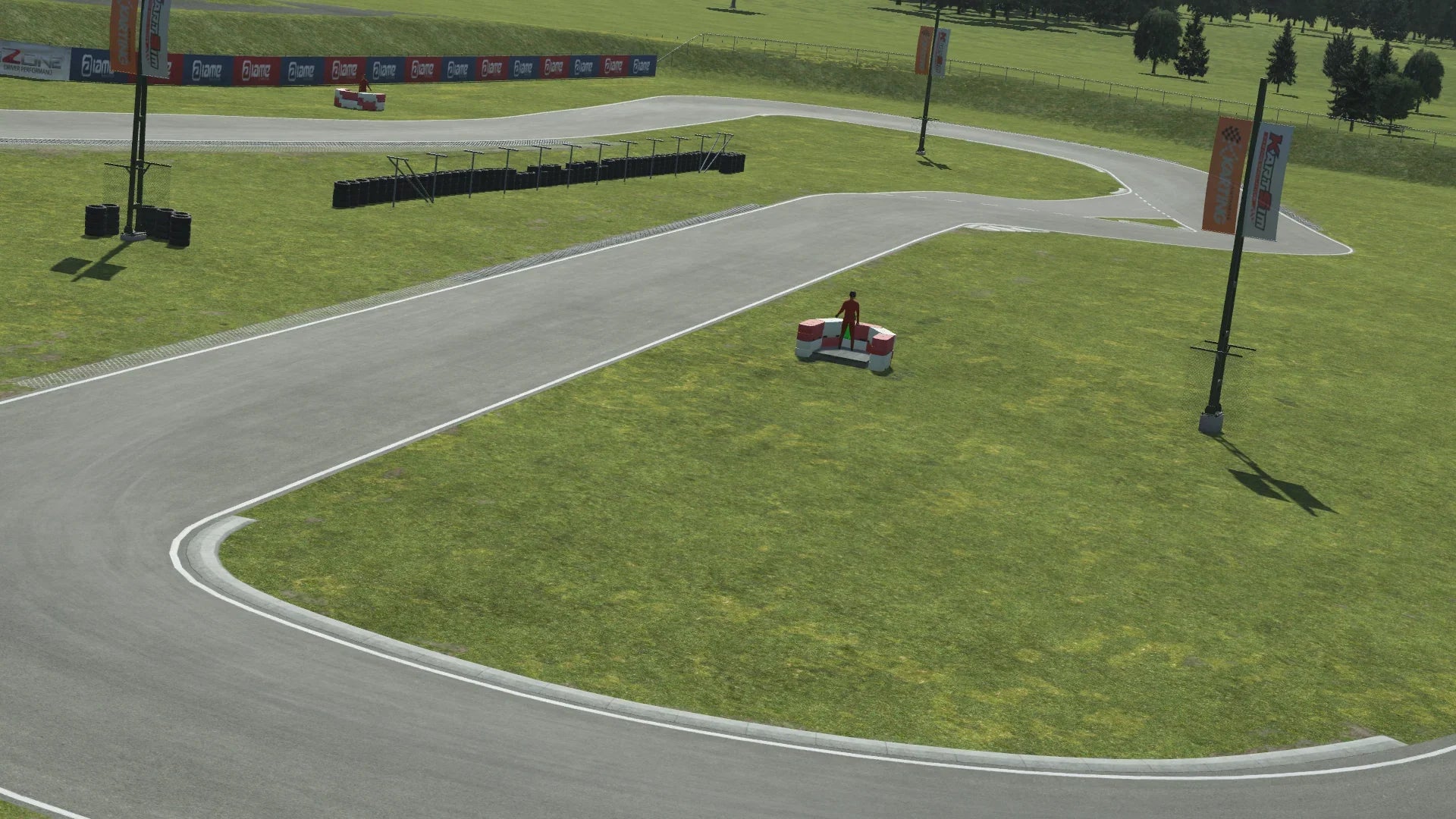 KartSim software render of the Kristianstad circuit: a smooth gray asphalt kart track winding through a grassy infield, with a small red model car on a tire barrier platform, scattered tire stacks, flag-branded banners on poles, and rolling trees in the background.