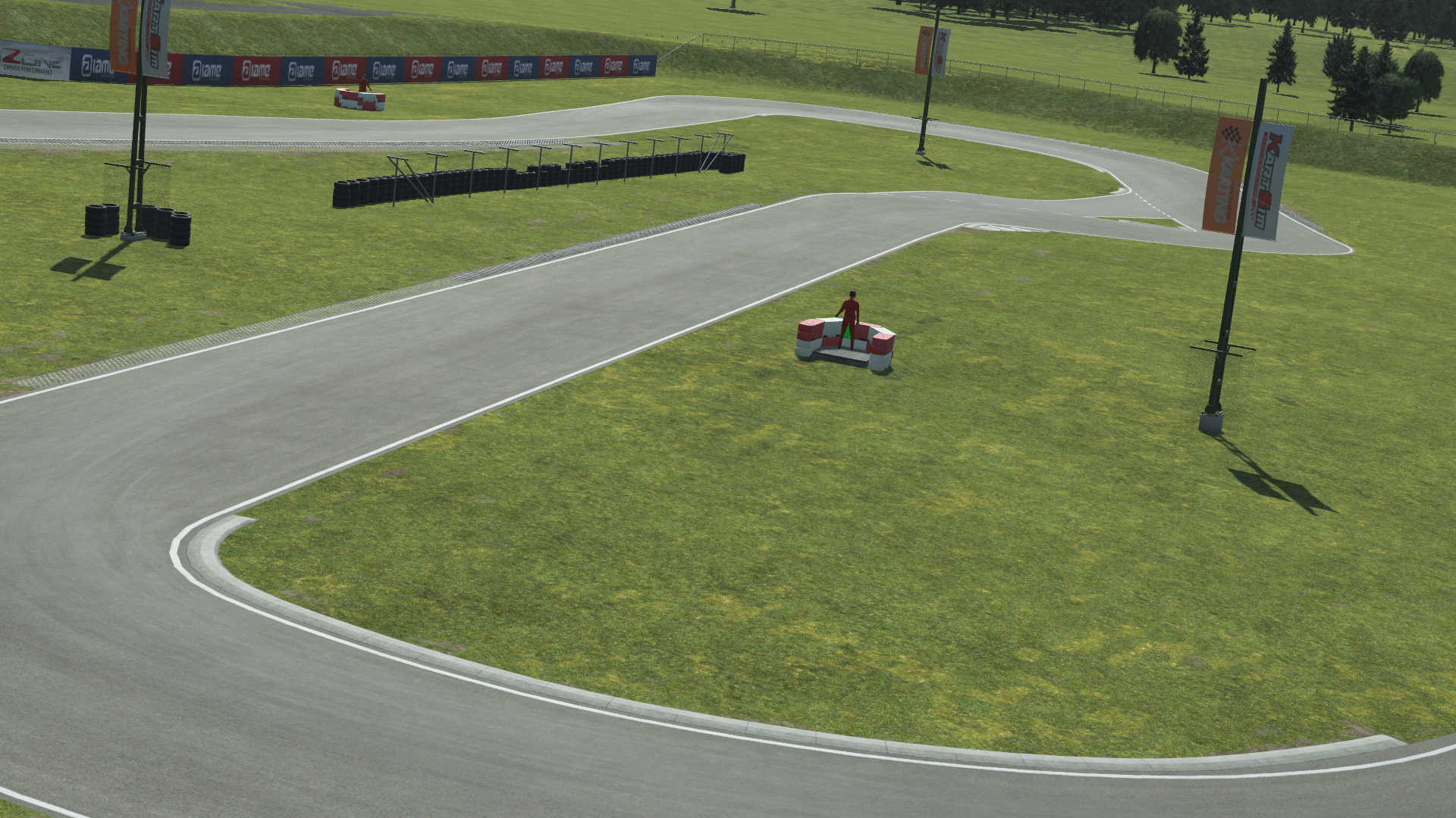 KartSim software render of the Kristianstad circuit: a smooth gray asphalt kart track winding through a grassy infield, with a small red model car on a tire barrier platform, scattered tire stacks, flag-branded banners on poles, and rolling trees in the background.