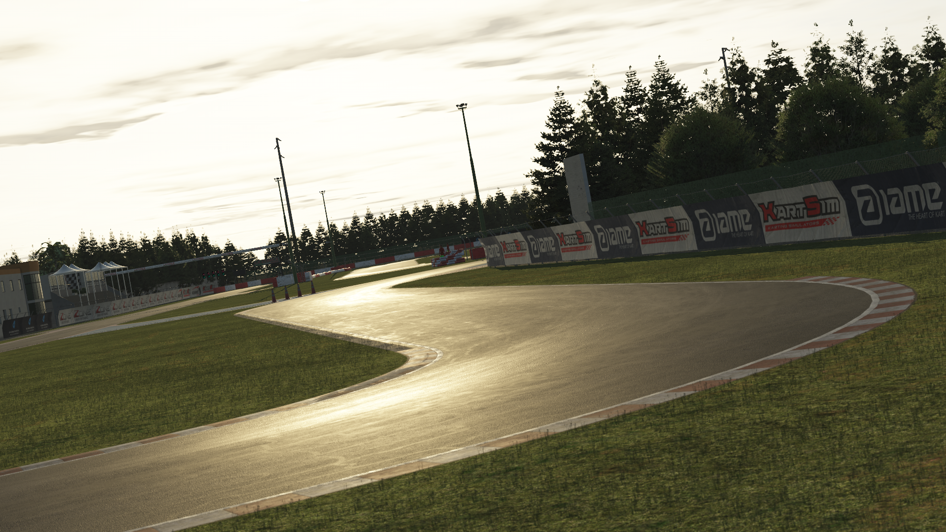 KartSim software screenshot of the La Conca kart track at dusk, showing a smooth asphalt curve glistening in the low sun, flanked by green grass, red-and-white kerbs, advertising banners along the barrier, tall floodlight poles, and a line of dark pine trees under a cloudy sky.