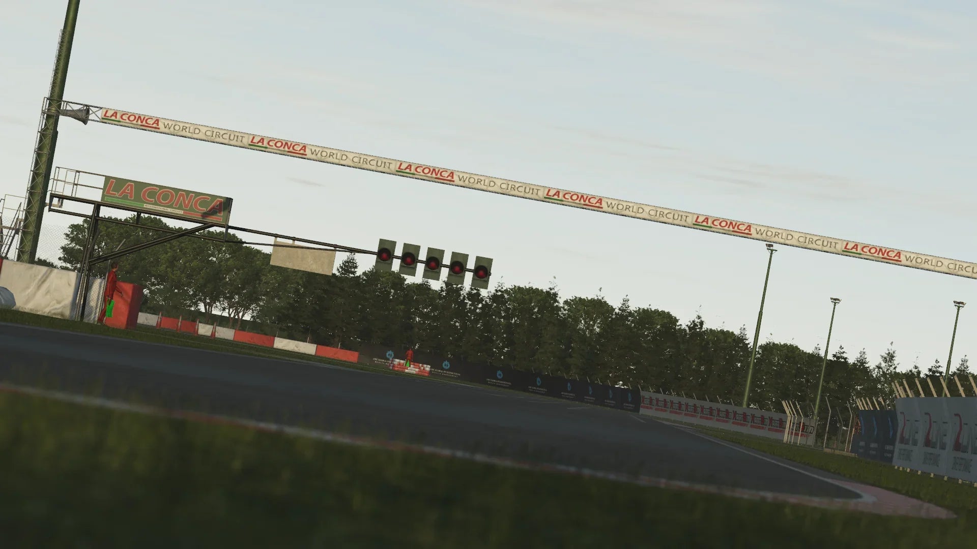 KartSim software render of the La Conca World Circuit’s start/finish straight, featuring the overhead “La Conca World Circuit” arch, a row of signal lights, red-and-white armco barriers, and a backdrop of dense trees under a pale sky.