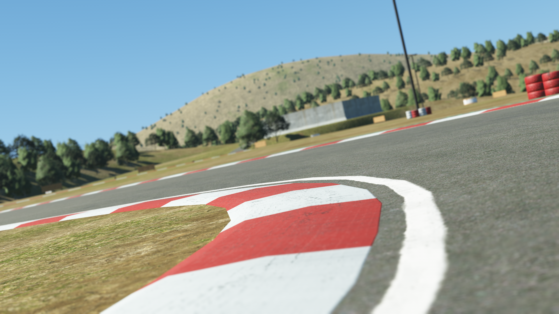 KartSim software rendering of Portimão kart track’s red-and-white kerb close-up, showing textured asphalt edge, dry grassy verge, and low hills under a clear blue sky.