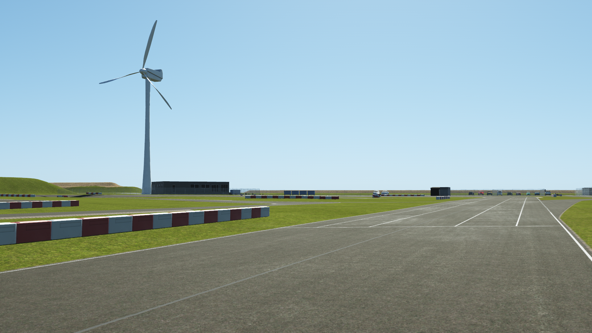KartSim software rendering of the Rodby kart track straightaway, featuring a tall wind turbine beside the asphalt and a grid of white start boxes, set against a clear blue sky and grassy infield.
