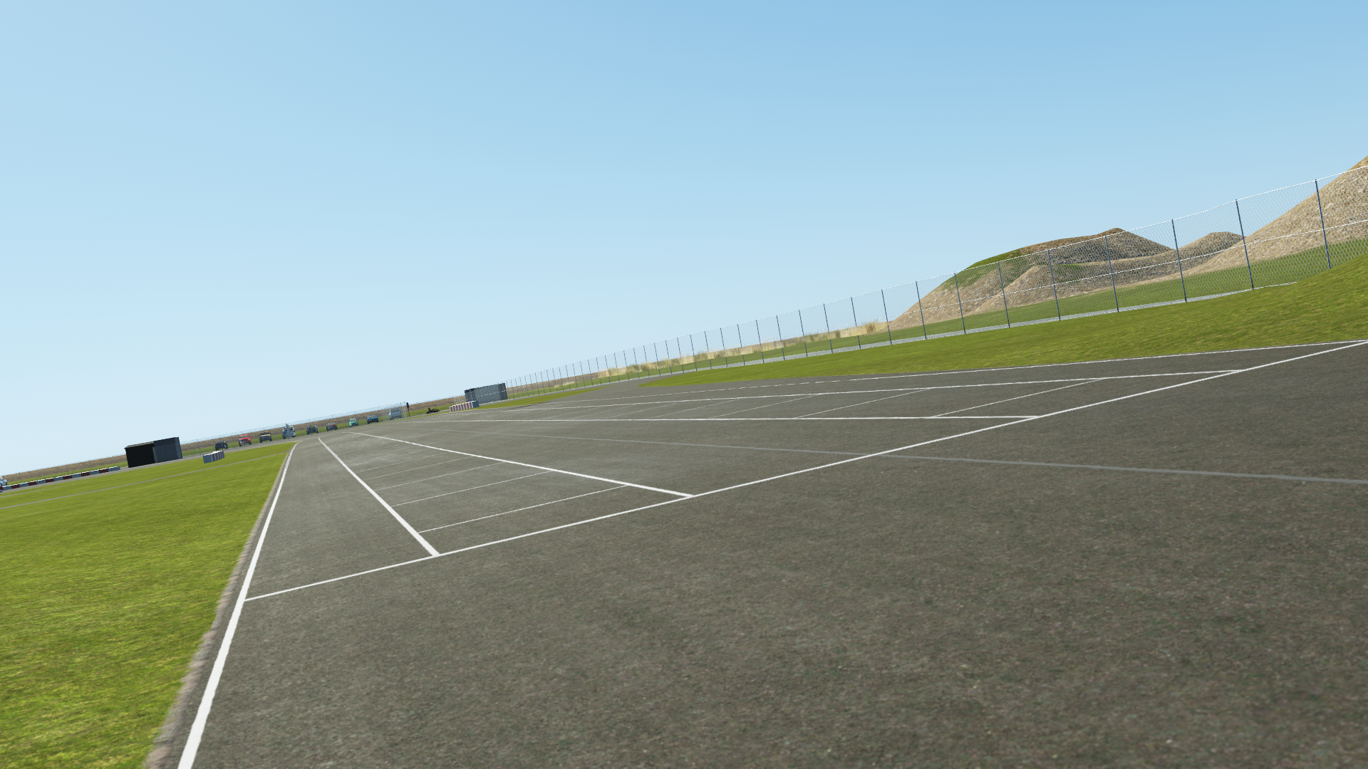 KartSim software rendering of the Rodby kart track start grid: an asphalt grid of white starting boxes alongside green grass, set against a clear blue sky and fencing in the distance.