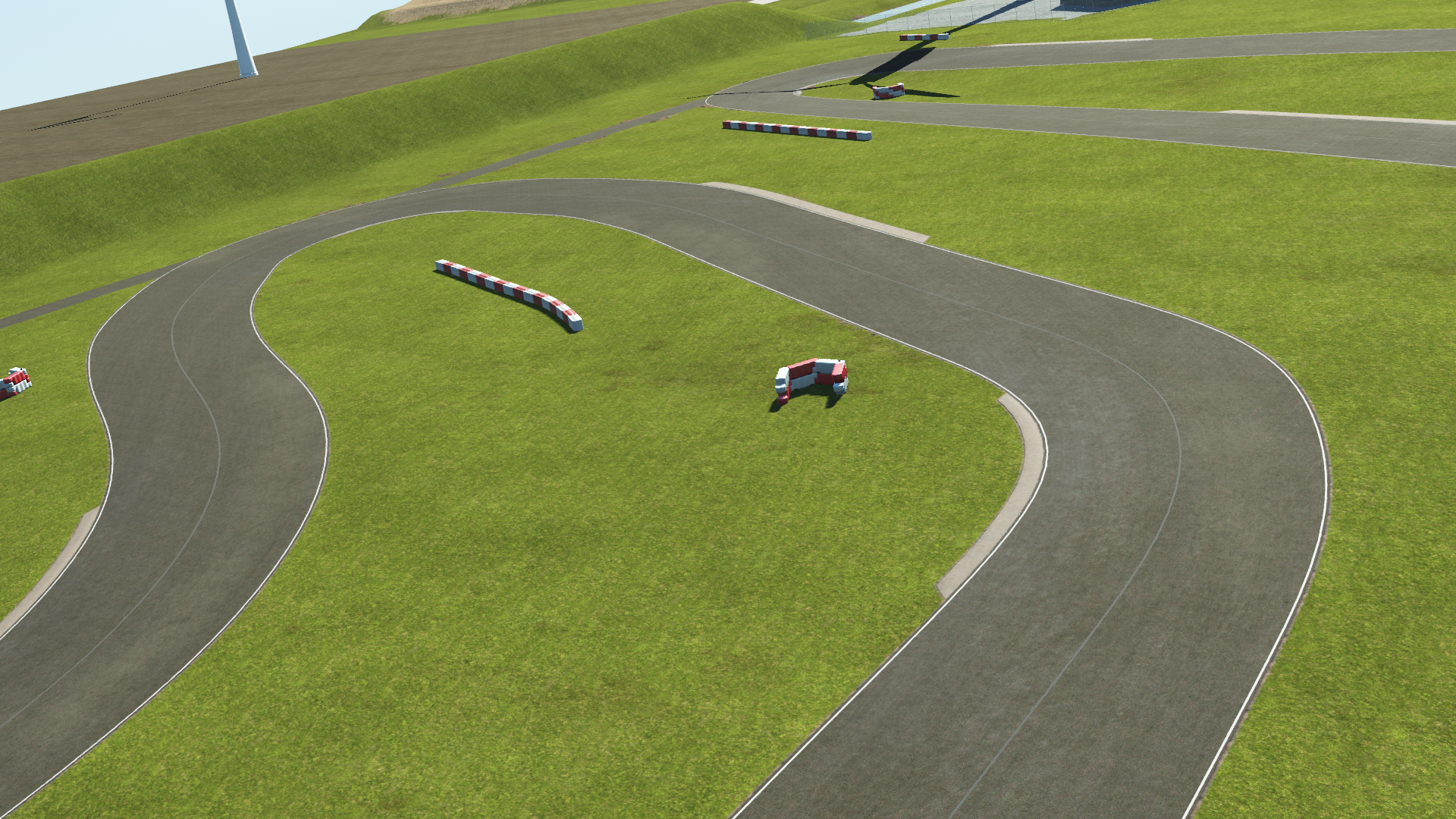 KartSim software rendering of the Rodby karting circuit showing a sweeping right-hand bend on an asphalt track surrounded by green grass run-off, red-and-white barrier segments placed on the infield, gentle grassy embankments, and a wind turbine base visible in the distance under a pale sky.