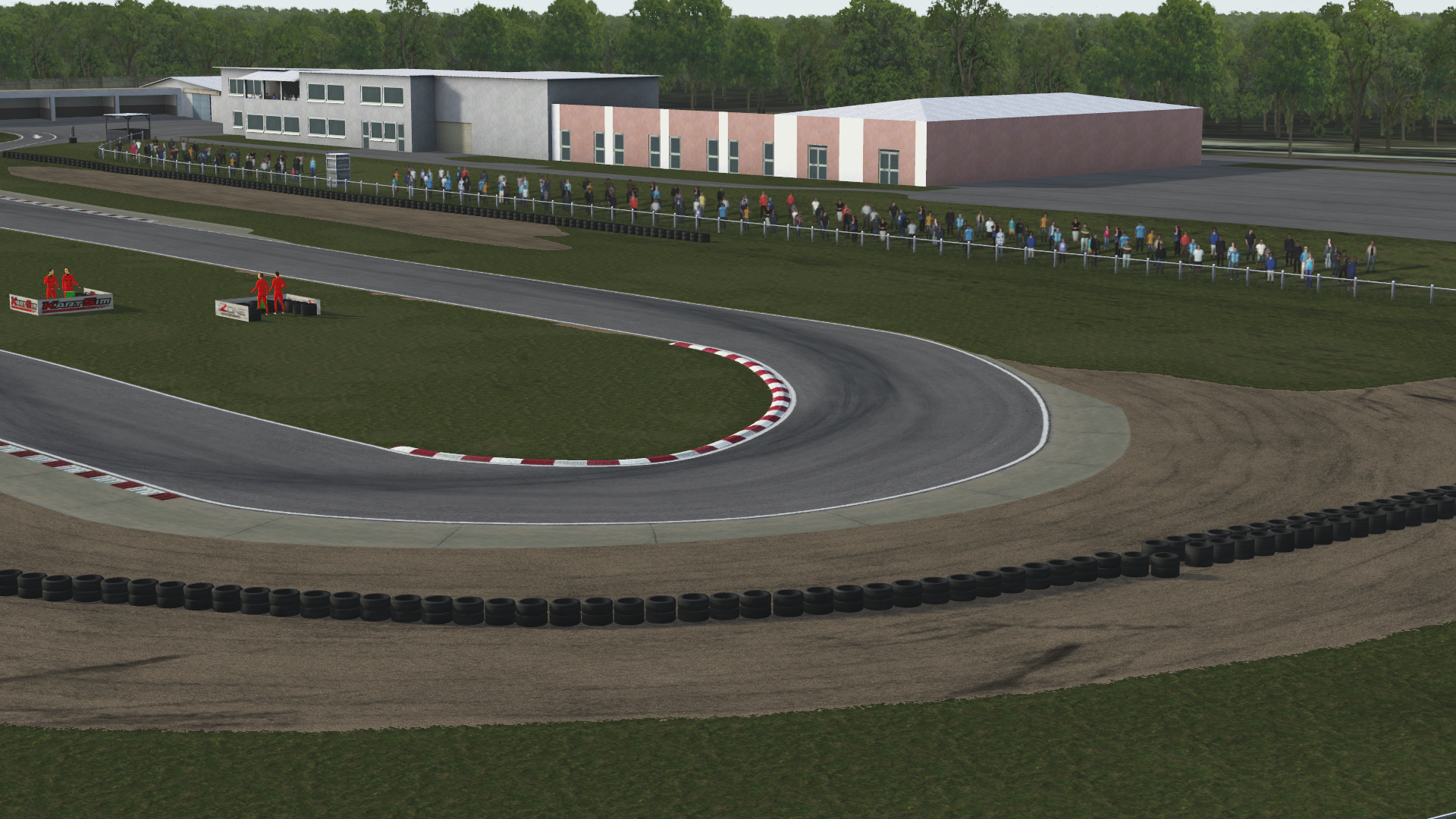 KartSim software rendering of the Salbris karting circuit, showing a sweeping left-hand corner with red-white kerbs, tire barriers on a gravel run-off, a line of spectators behind a guardrail, and pit buildings nestled among trees in the background.