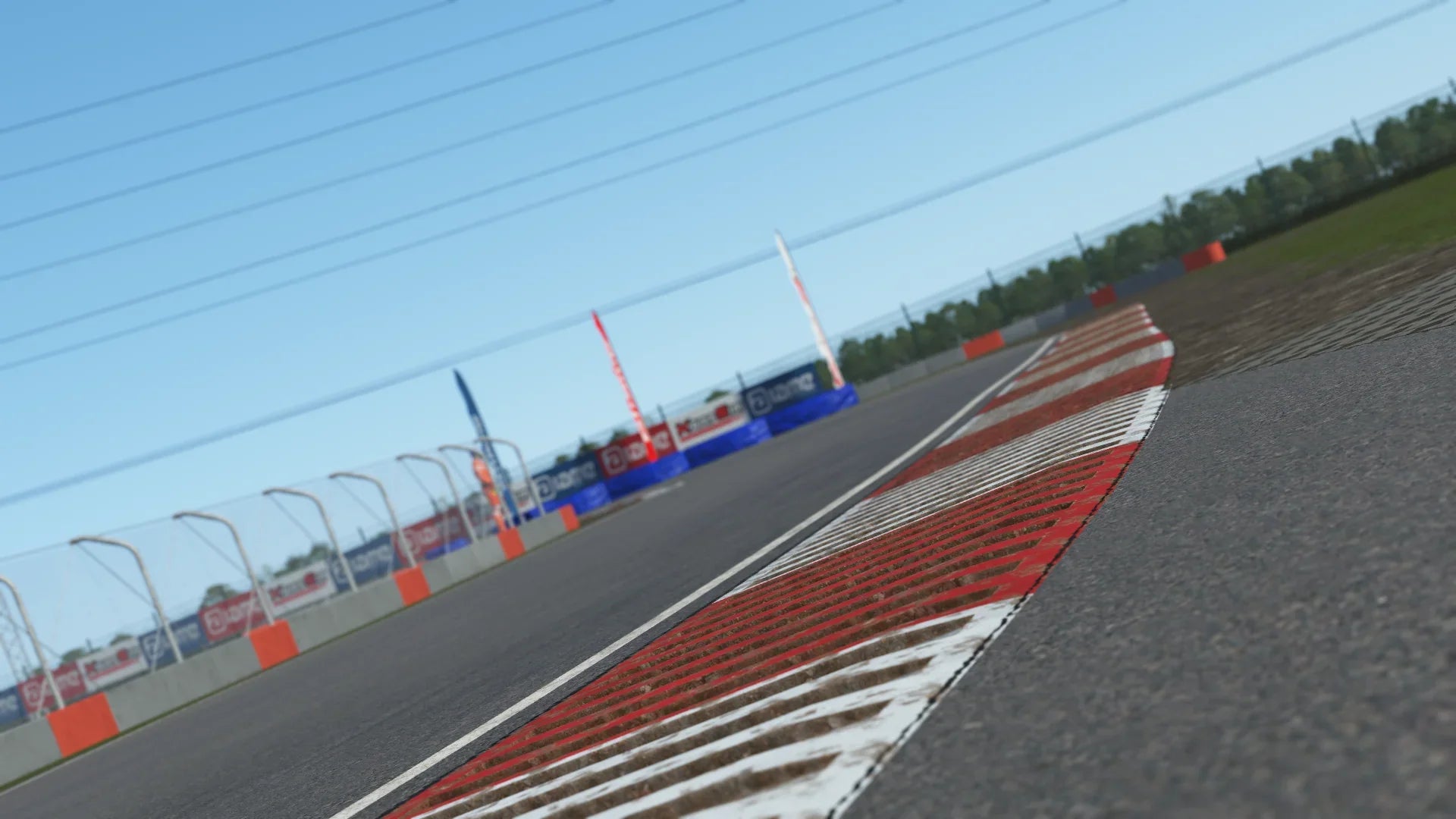 Close-up in-simulation view of a curb section at the Slovakiaring karting circuit in KartSim software, showing the red-white striped kerb, protective barriers with KartSim and Aliant banners, asphalt track surface, and clear blue sky.