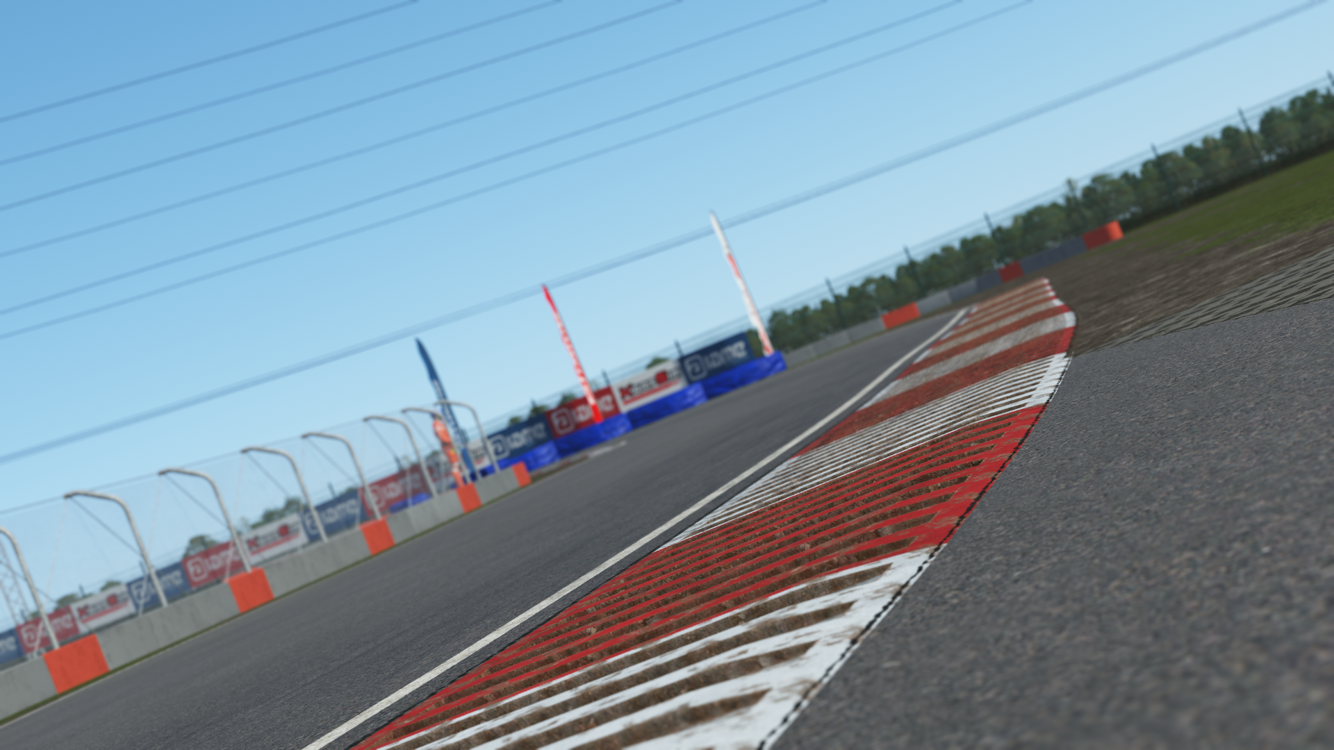 Close-up in-simulation view of a curb section at the Slovakiaring karting circuit in KartSim software, showing the red-white striped kerb, protective barriers with KartSim and Aliant banners, asphalt track surface, and clear blue sky.