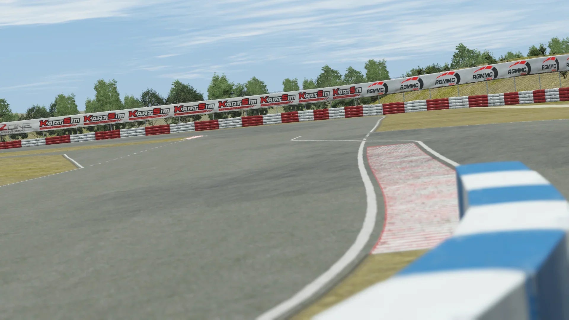 Close-up in-simulation view of the Valencia karting circuit in KartSim software, focused on the asphalt track with red-white kerbs, blue-white tire barrier, KartSim-branded trackside hoardings, and grass run-off areas under a clear sky.