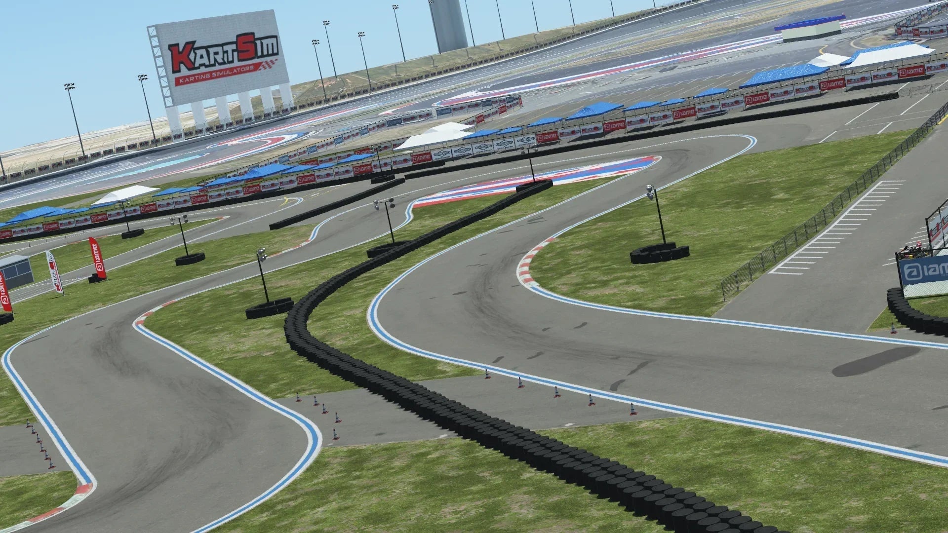 Wide view of a karting circuit with tire barriers, sponsor banners, and a large KartSim billboard under a blue sky