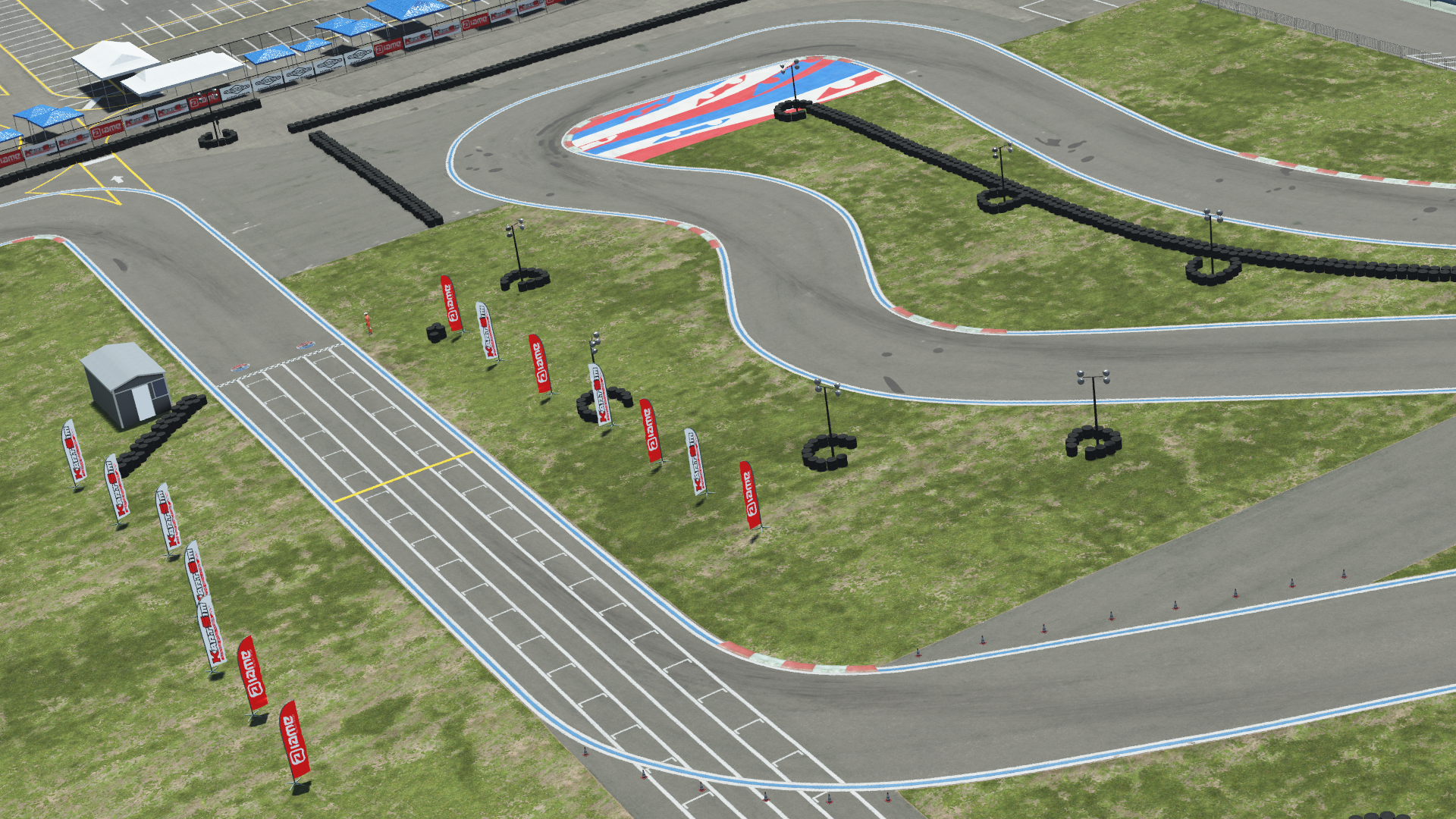 Overhead view of a karting track with tire barriers, grid markings, and sponsor flags on a grassy field