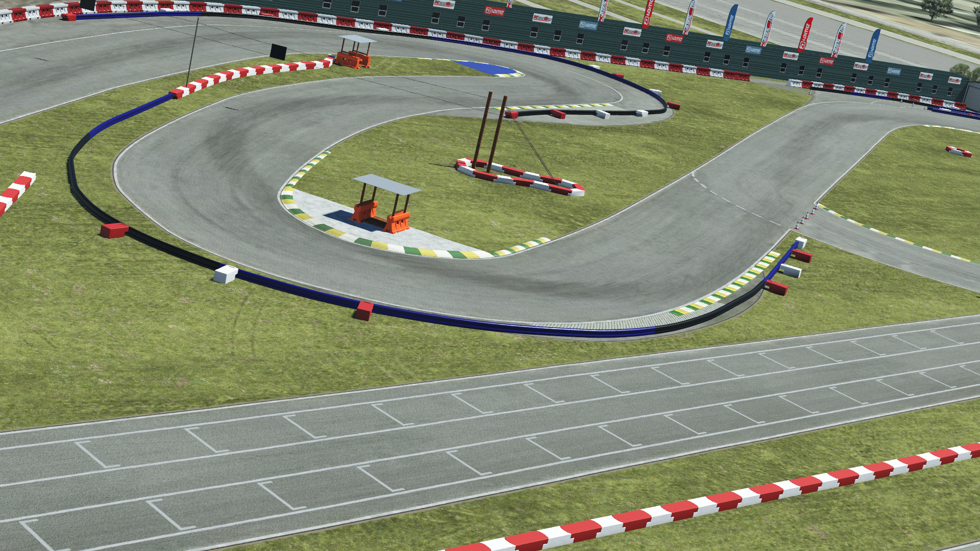 Go-kart track with sweeping turns, red and white barriers, grassy infield, and paddock fencing under a clear sky
