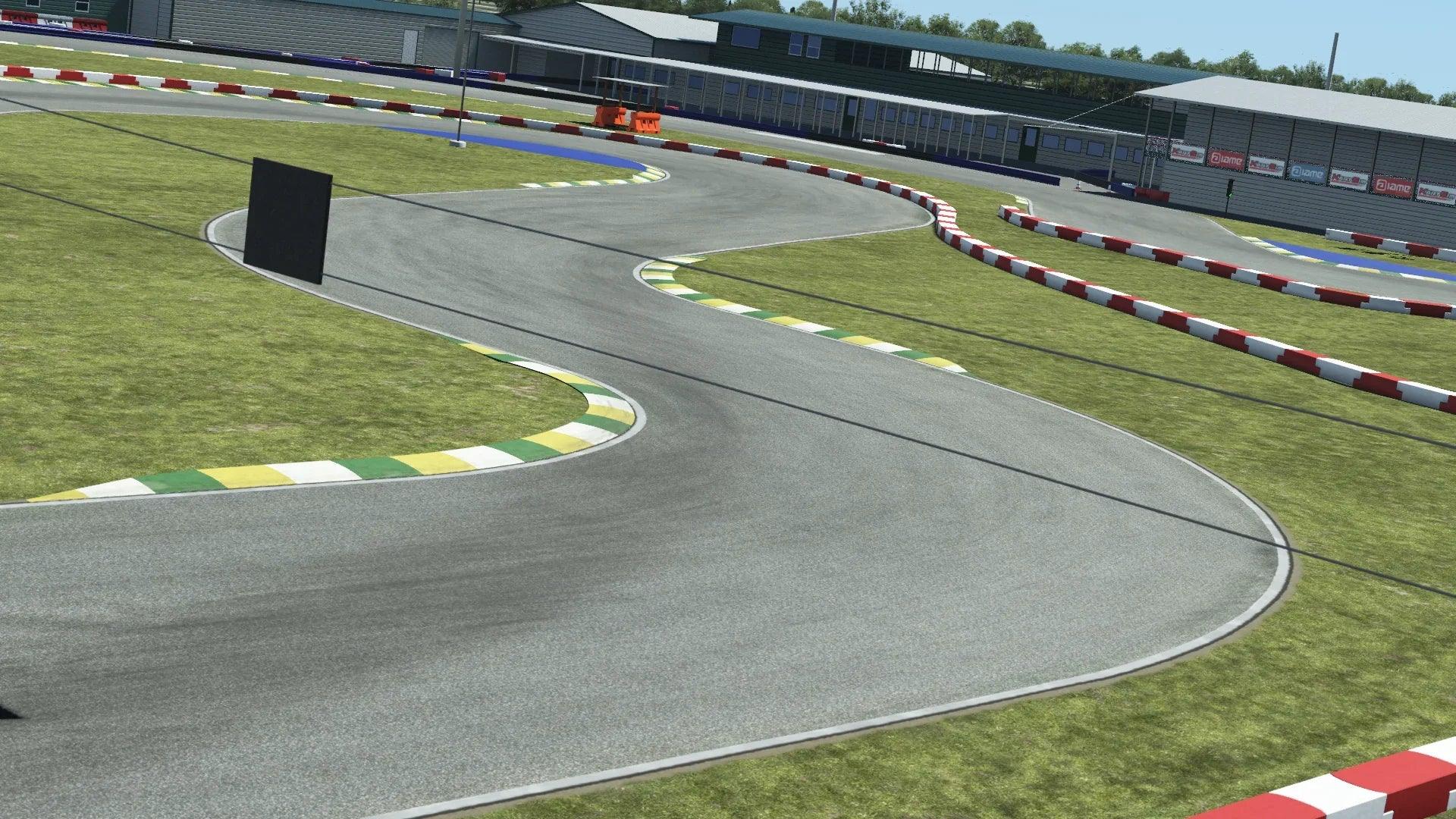 Go-kart track featuring tight S-turns, grass run-offs, and curb markings near a modern paddock building