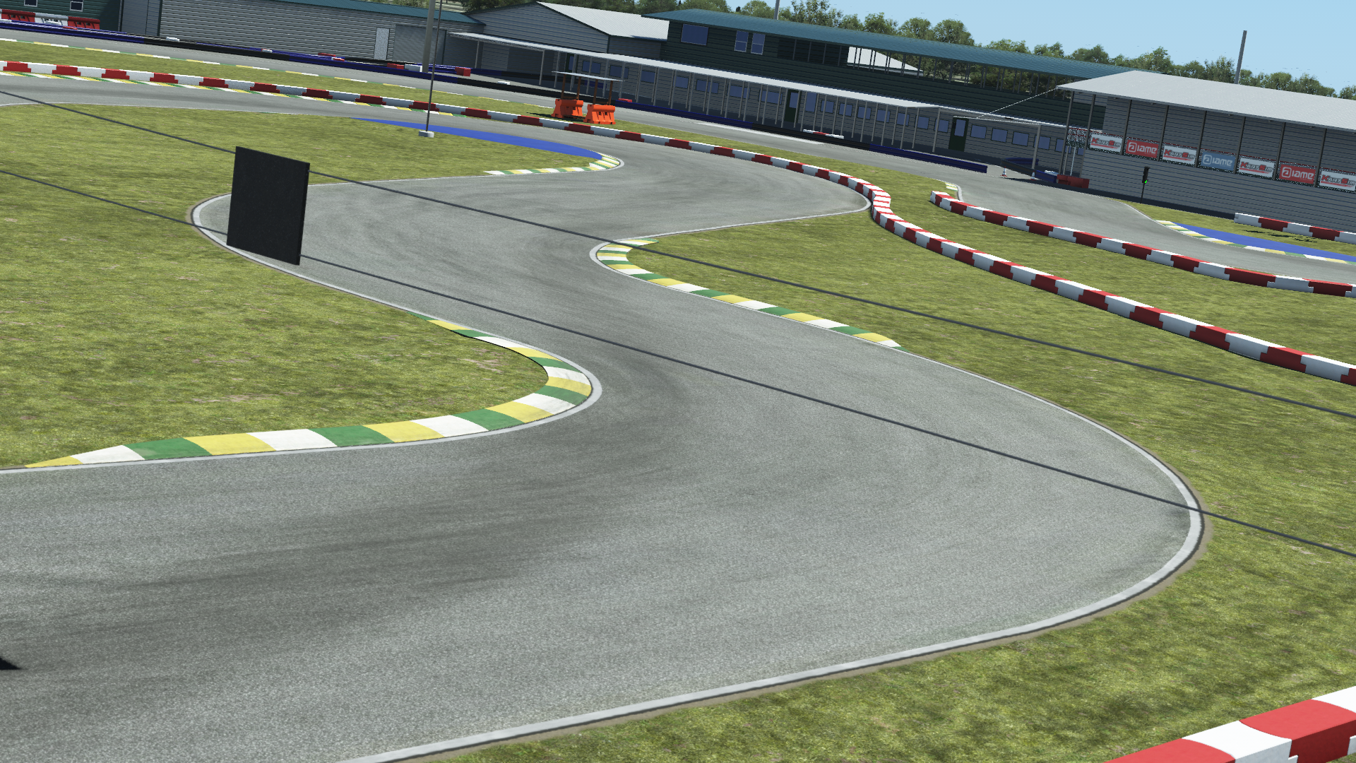 Go-kart track featuring tight S-turns, grass run-offs, and curb markings near a modern paddock building