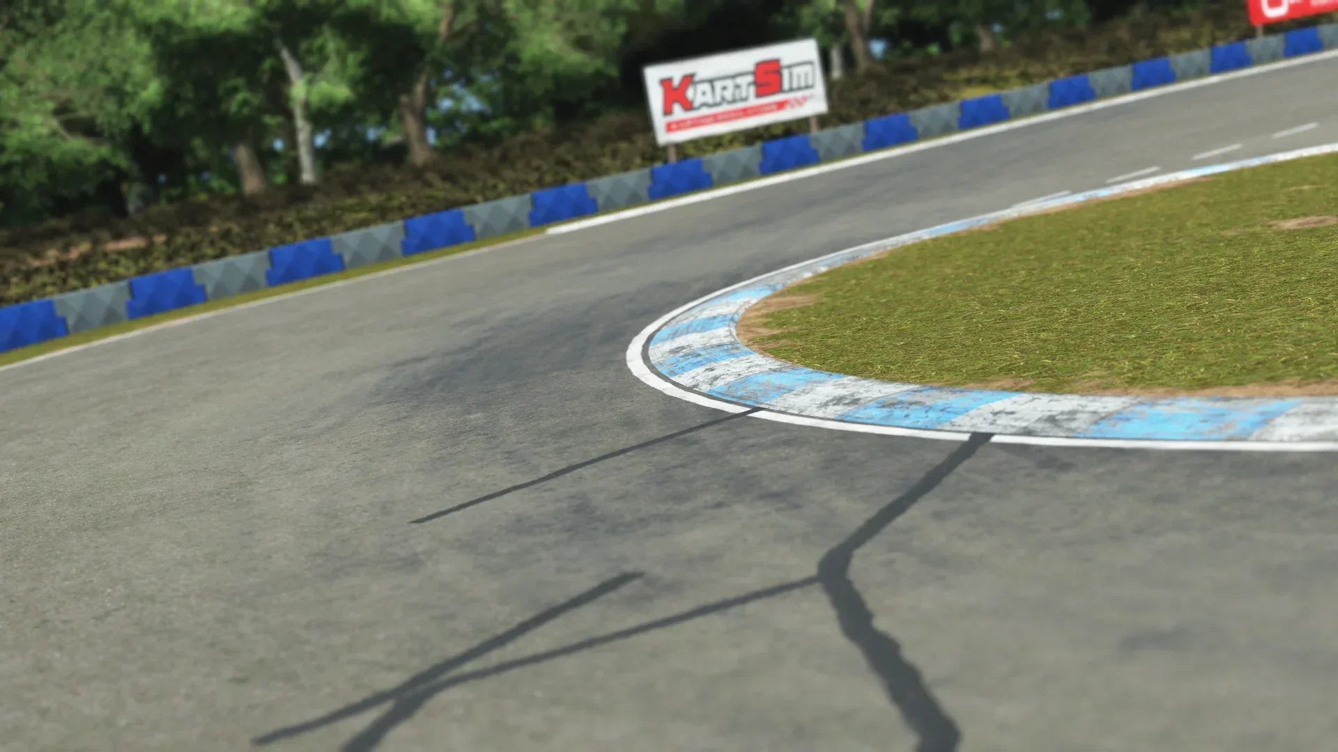 Close-up of a karting track corner with blue and gray barriers, white-and-blue kerb, and a KartSim sign in the background