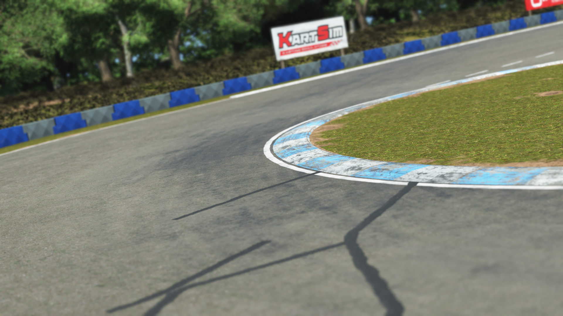 Close-up of a karting track corner with blue and gray barriers, white-and-blue kerb, and a KartSim sign in the background