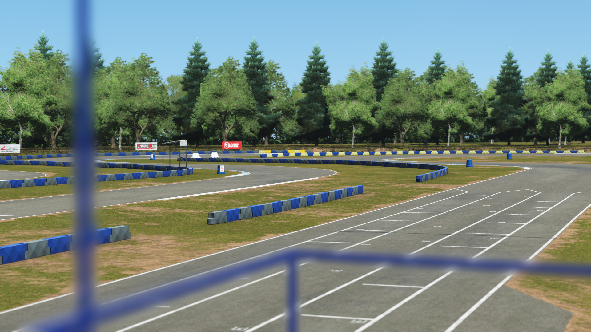 Wide shot of Greg Moore kart track with blue plastic barriers, trees in the background, and fencing visible in the foreground