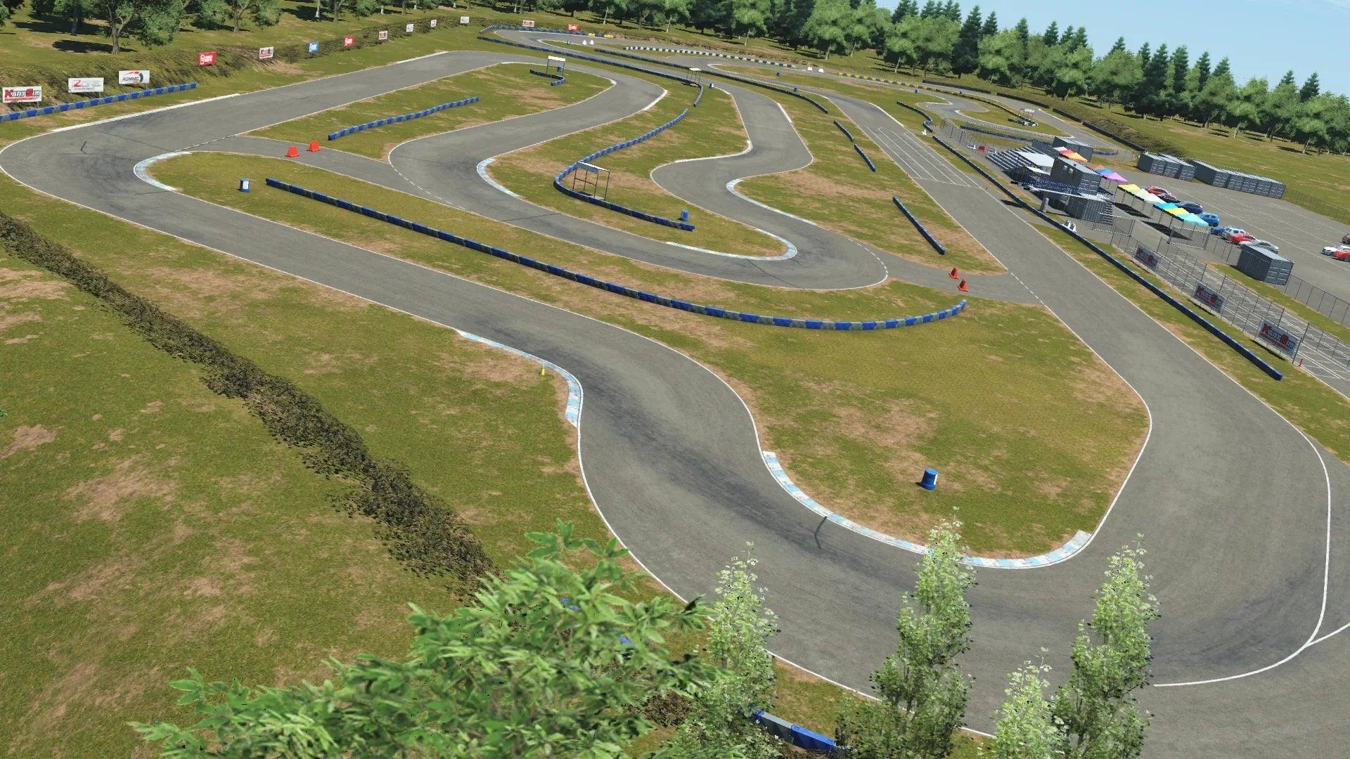 Wide aerial view of Greg Moore karting circuit with winding turns, blue barriers, grassy patches, and parked cars near the paddock area
