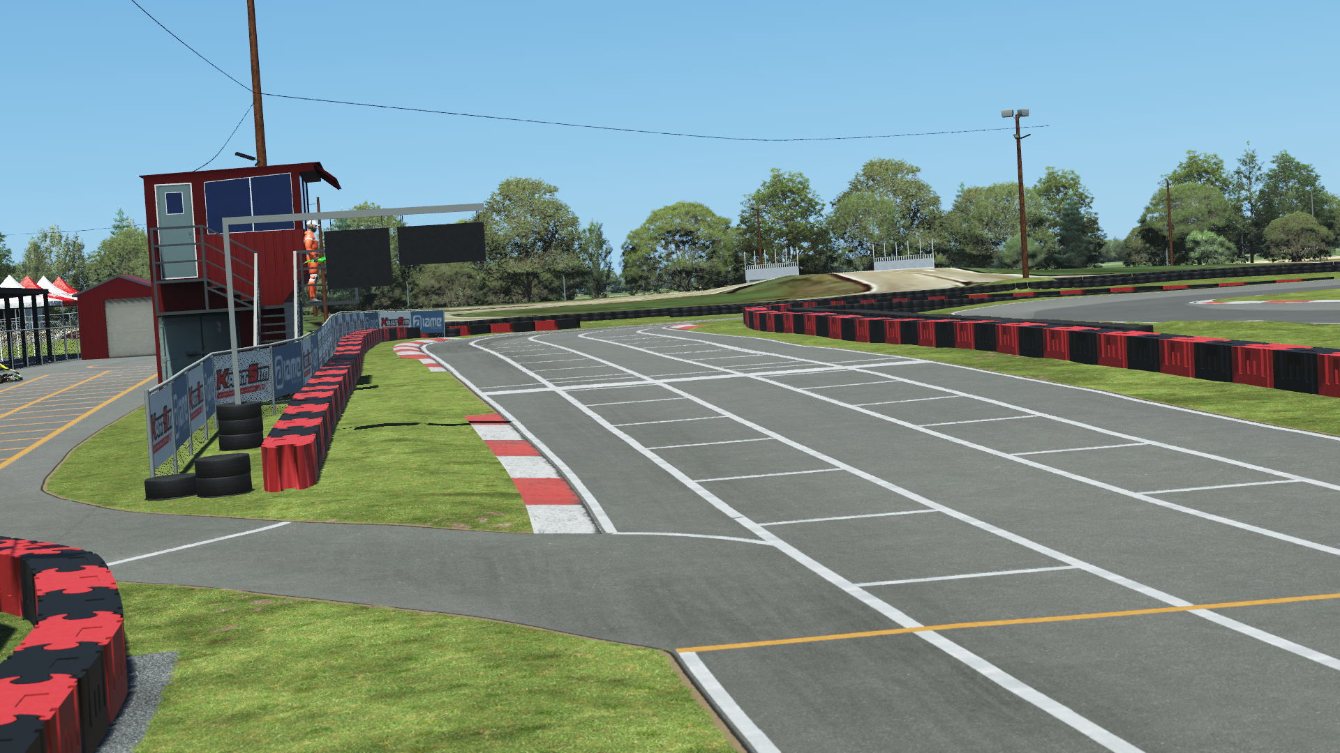 Hamilton karting track starting grid with red barriers, grass, and trees on a sunny day