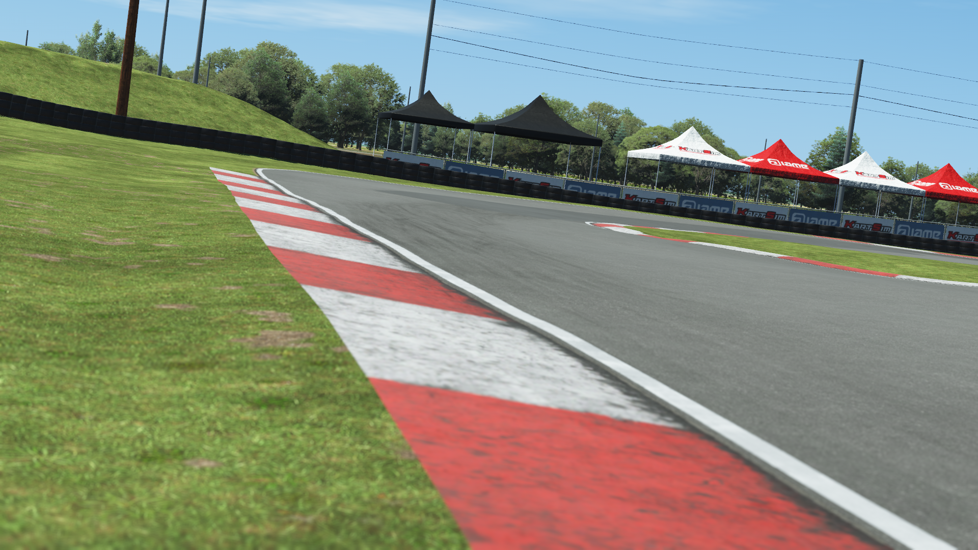 Hamilton kart track with red and white curb, grassy runoff area, and tents under clear sky