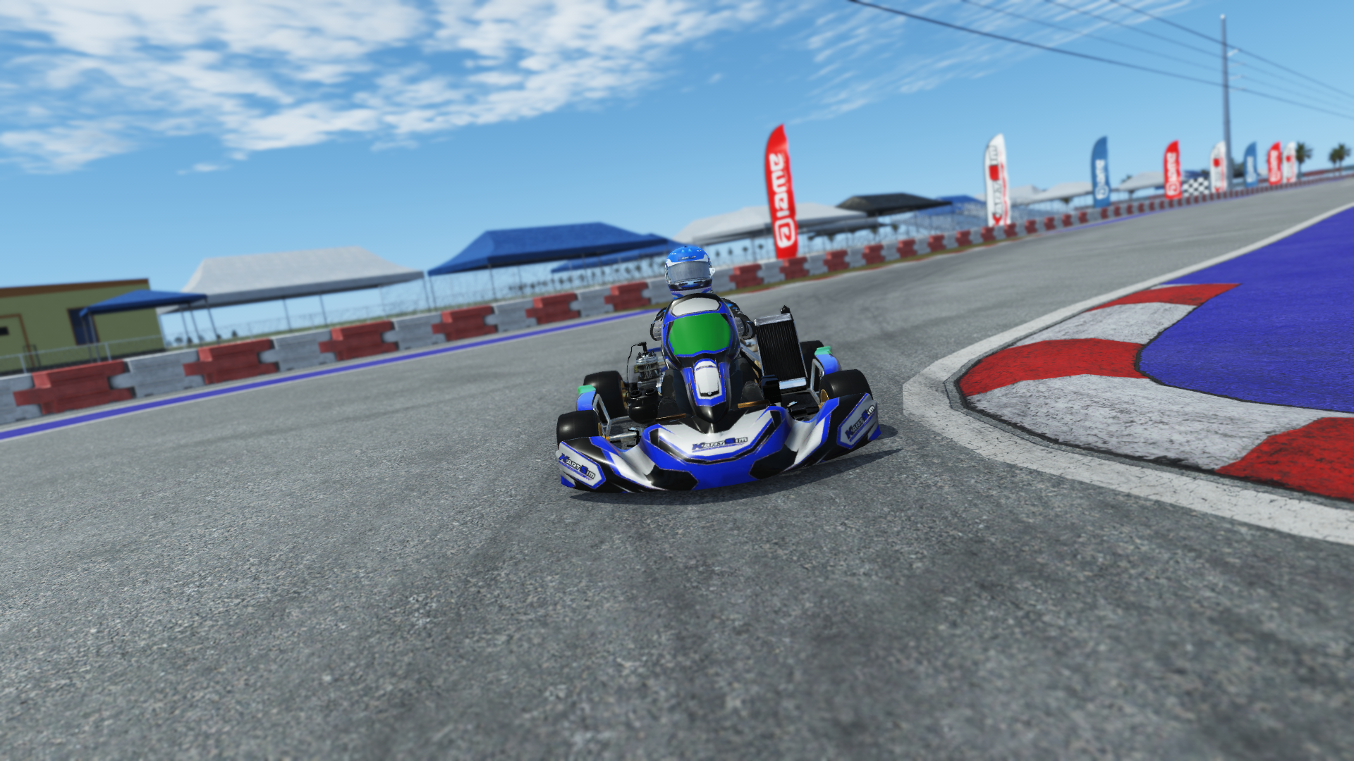 IAME X30 Junior US 007 kart with blue, white, and yellow livery on karting track with tire barriers