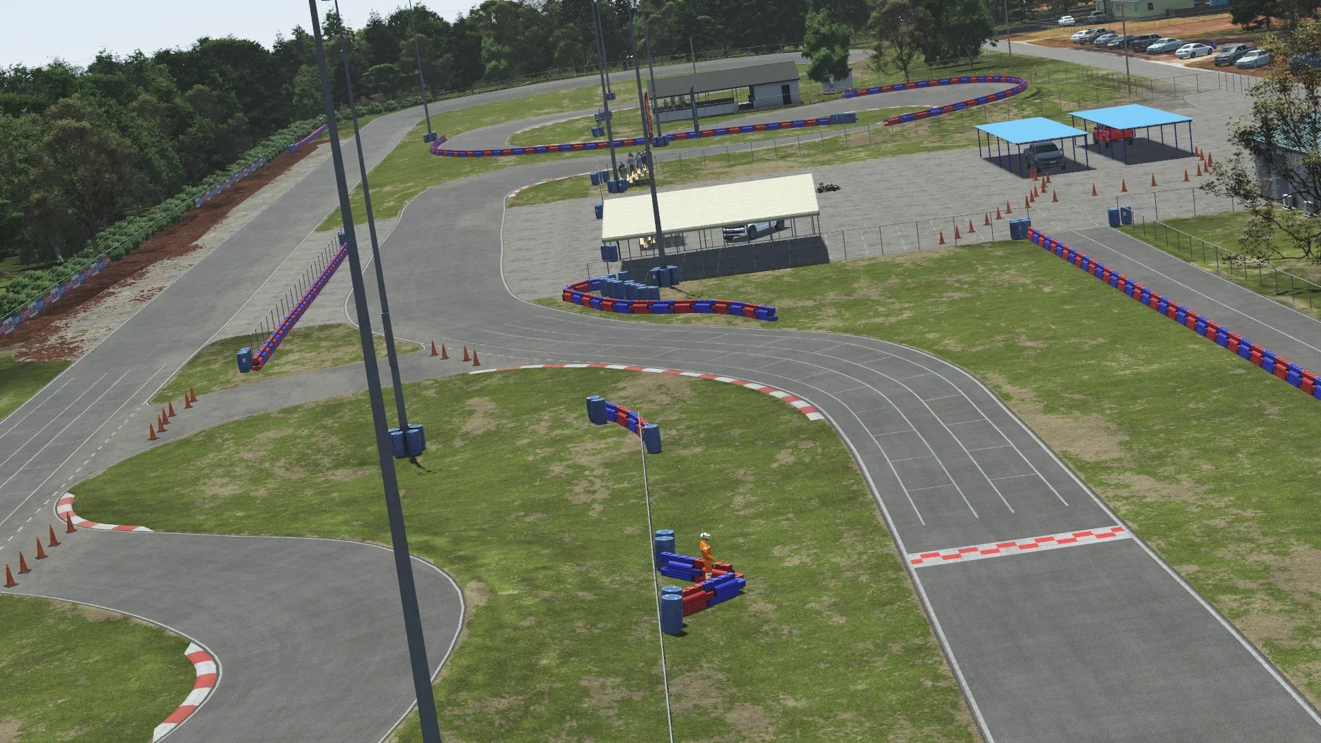 Jacksonville karting circuit paddock view – red and blue barrier-lined turns, pit tents, grid markings, and support buildings