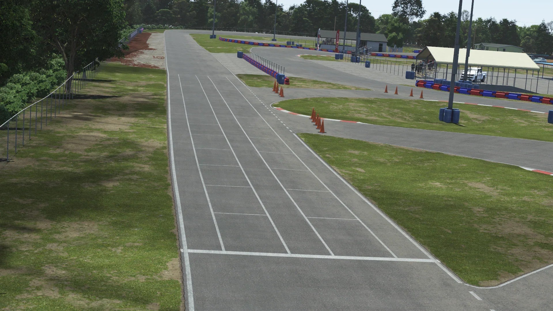 Start/finish straight at Jacksonville karting circuit with grid markings, cones, and red-blue barriers under clear skies