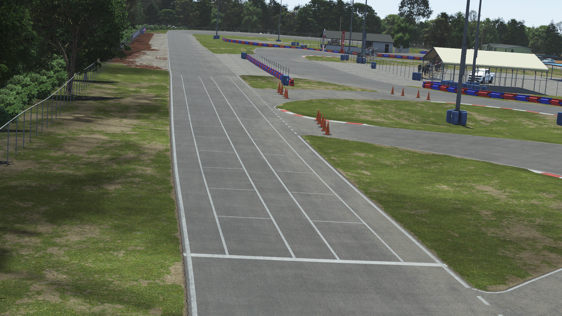 Start/finish straight at Jacksonville karting circuit with grid markings, cones, and red-blue barriers under clear skies