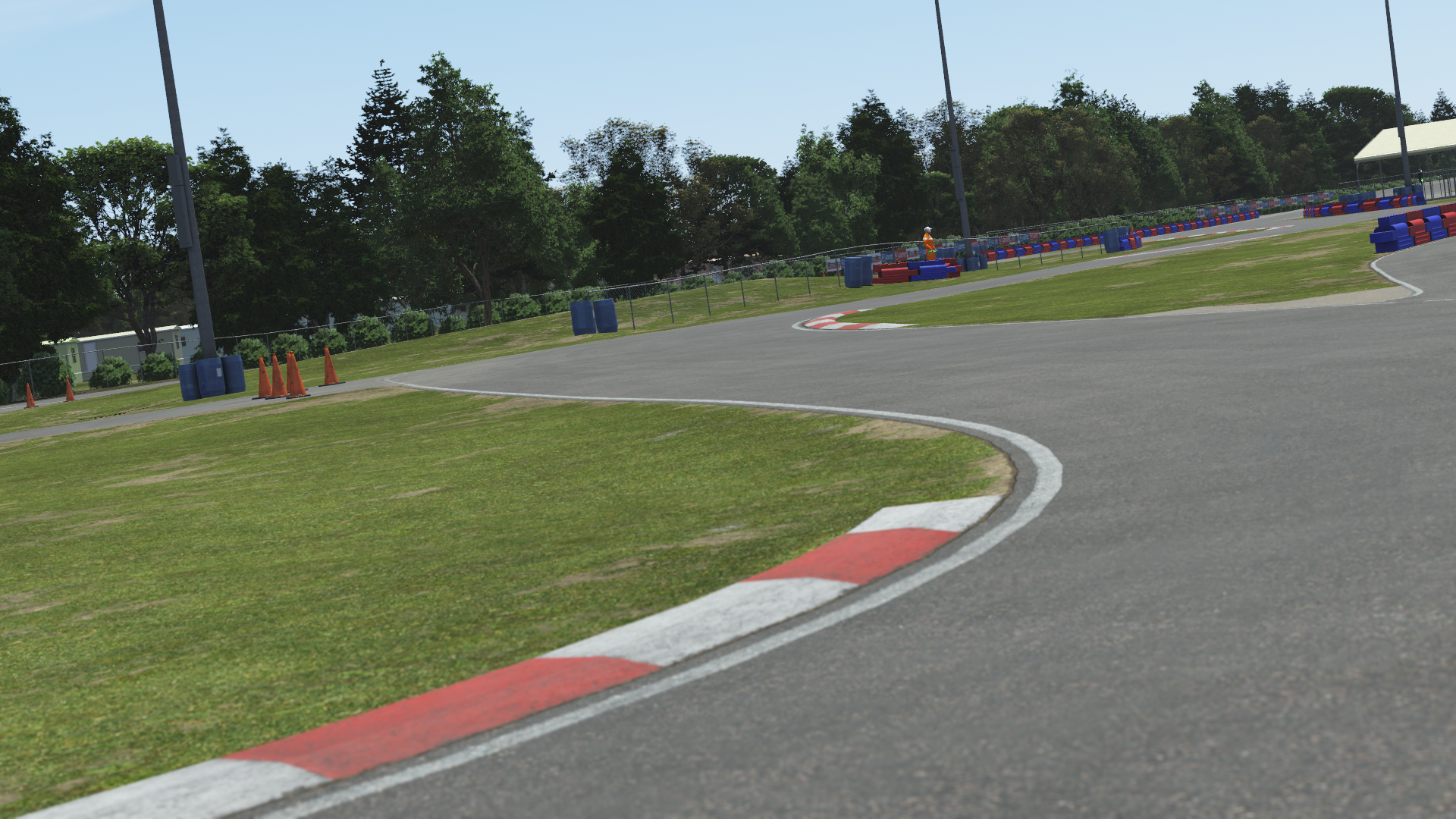 Karting circuit turn with curbing, grass, and trees in the background on a sunny day