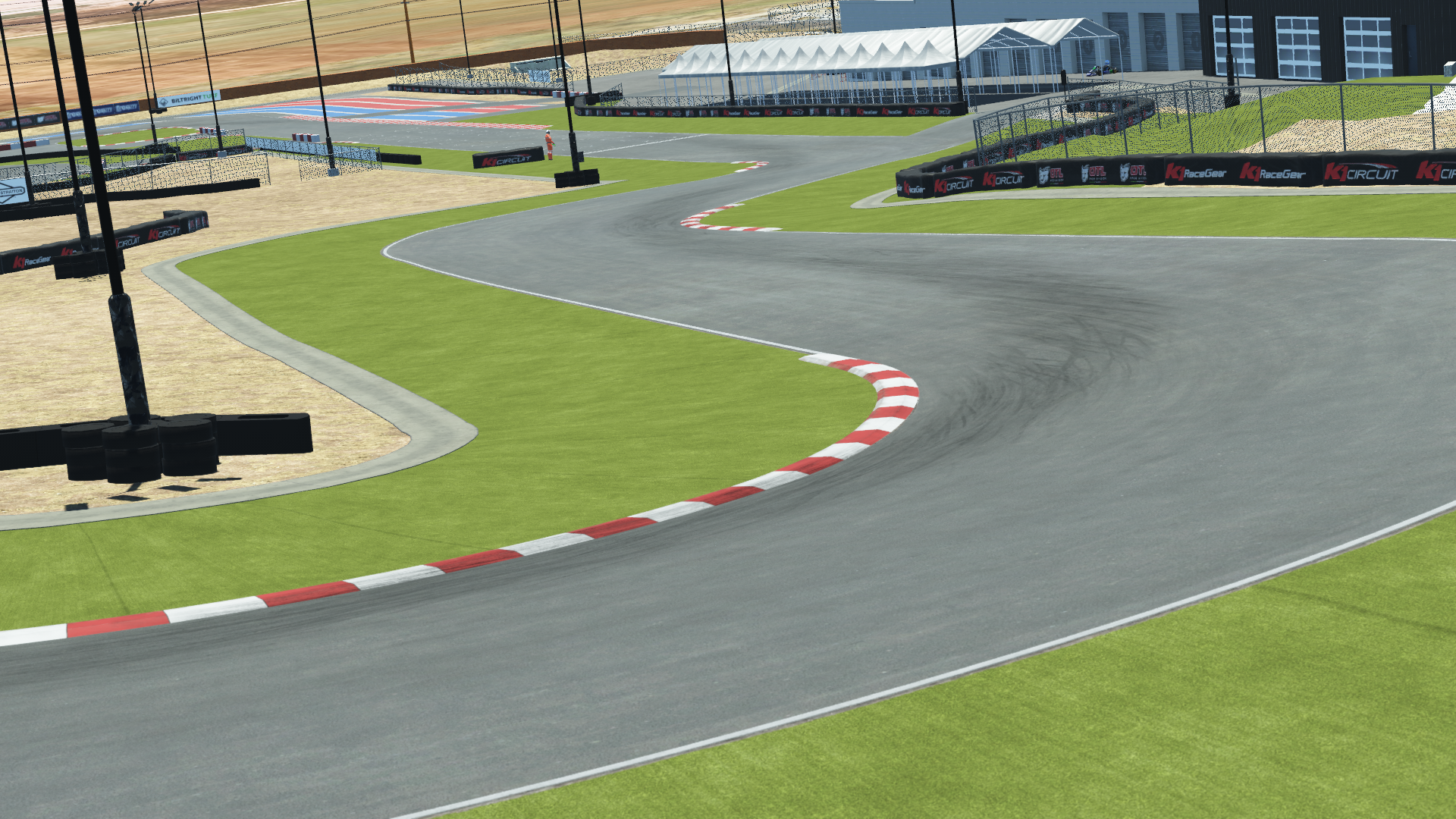 K1 Winchester karting track corner – red and white curbs, turf runoff, tire marks, and paddock tents in the background
