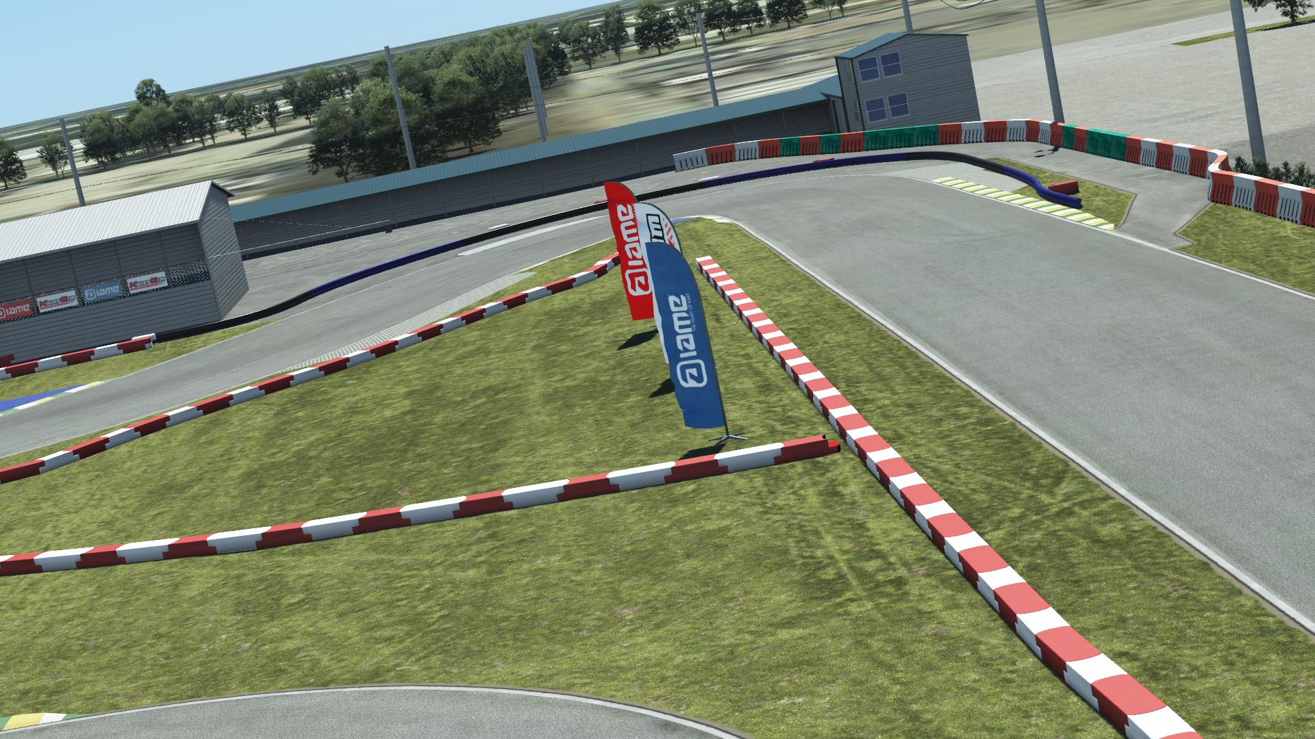 Go-kart circuit with red and white barriers, grassy verge, and branded flags in an open paddock setting