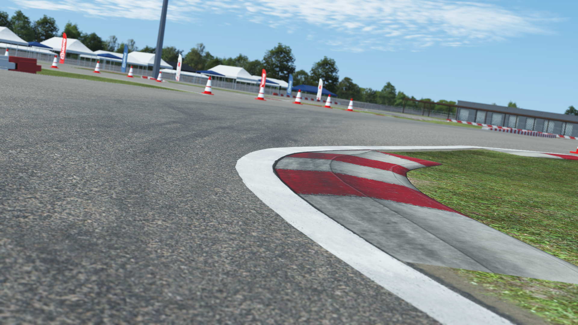 Close-up view of a karting track corner with red and white curb, cones, and event tents in the background on a clear day