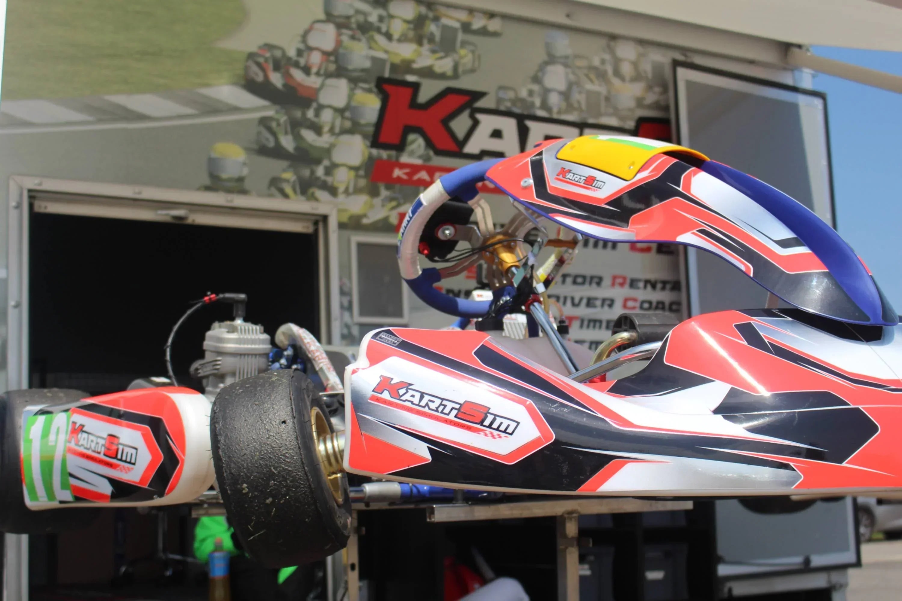 KartSim on-track driver coaching setup showing a real kart with branding in front of the team trailer, highlighting integration of simulation with real-world racing support