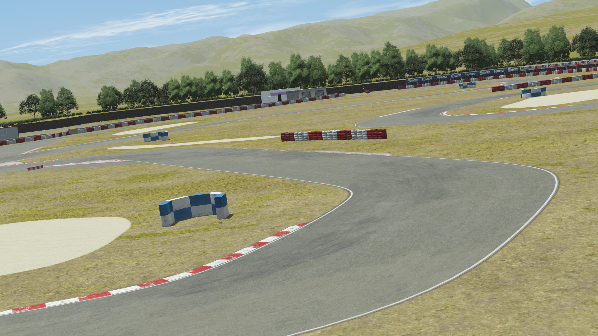 View of the Valencia karting circuit in KartSim software, showing a sweeping asphalt curve with red-white kerbs, grass run-off areas, tire barrier markers, surrounding dry grass landscape, and distant hills under a blue sky.
